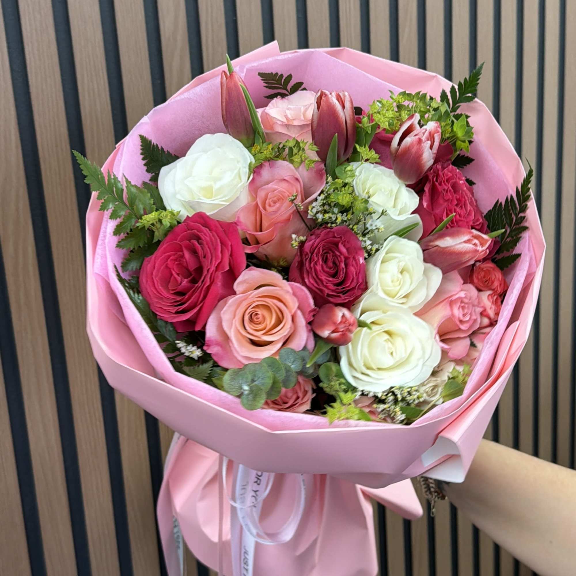 Pink-wrapped bouquet of roses and tulips in pink, white, and red