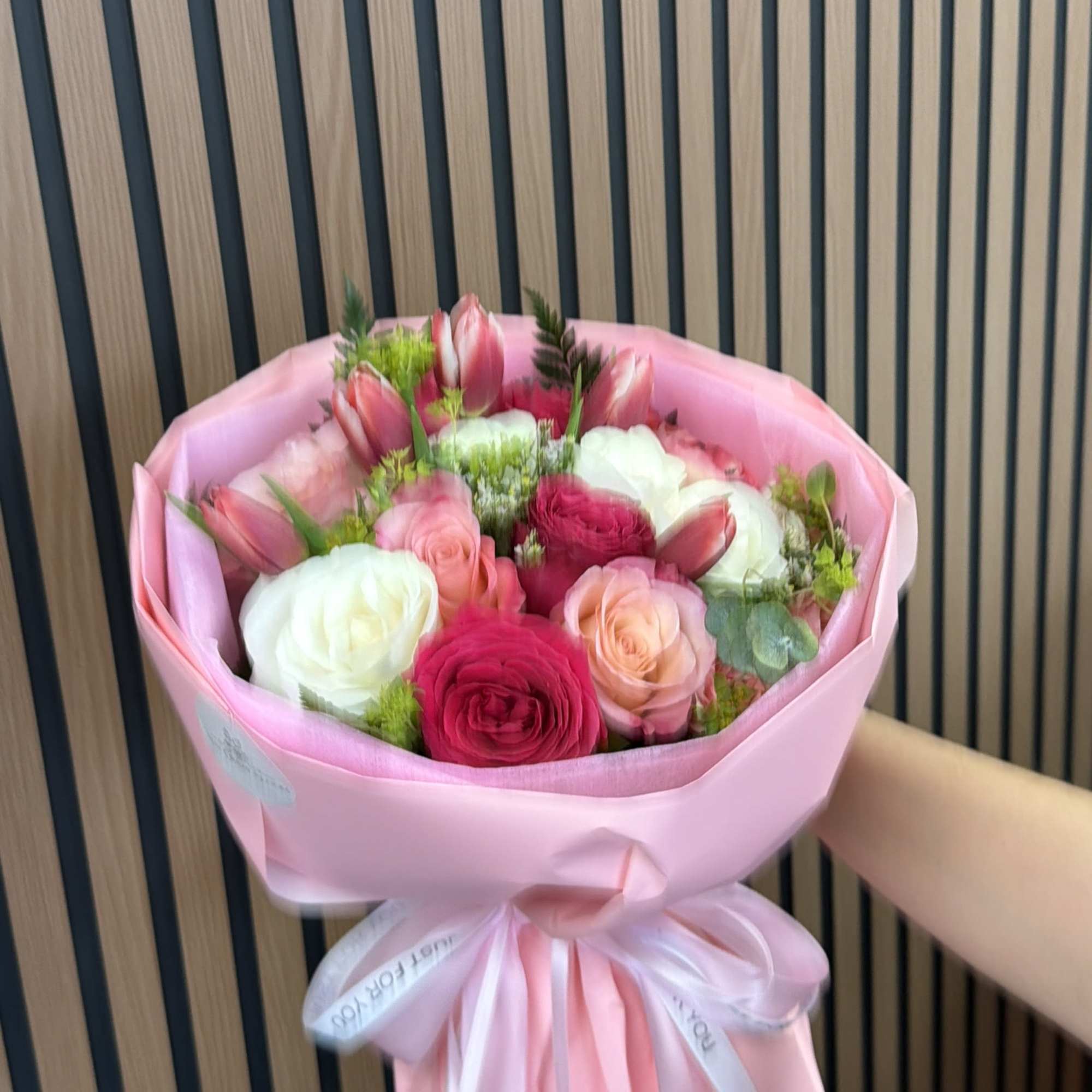 Pink-wrapped bouquet of roses and tulips in pink, white, and peach