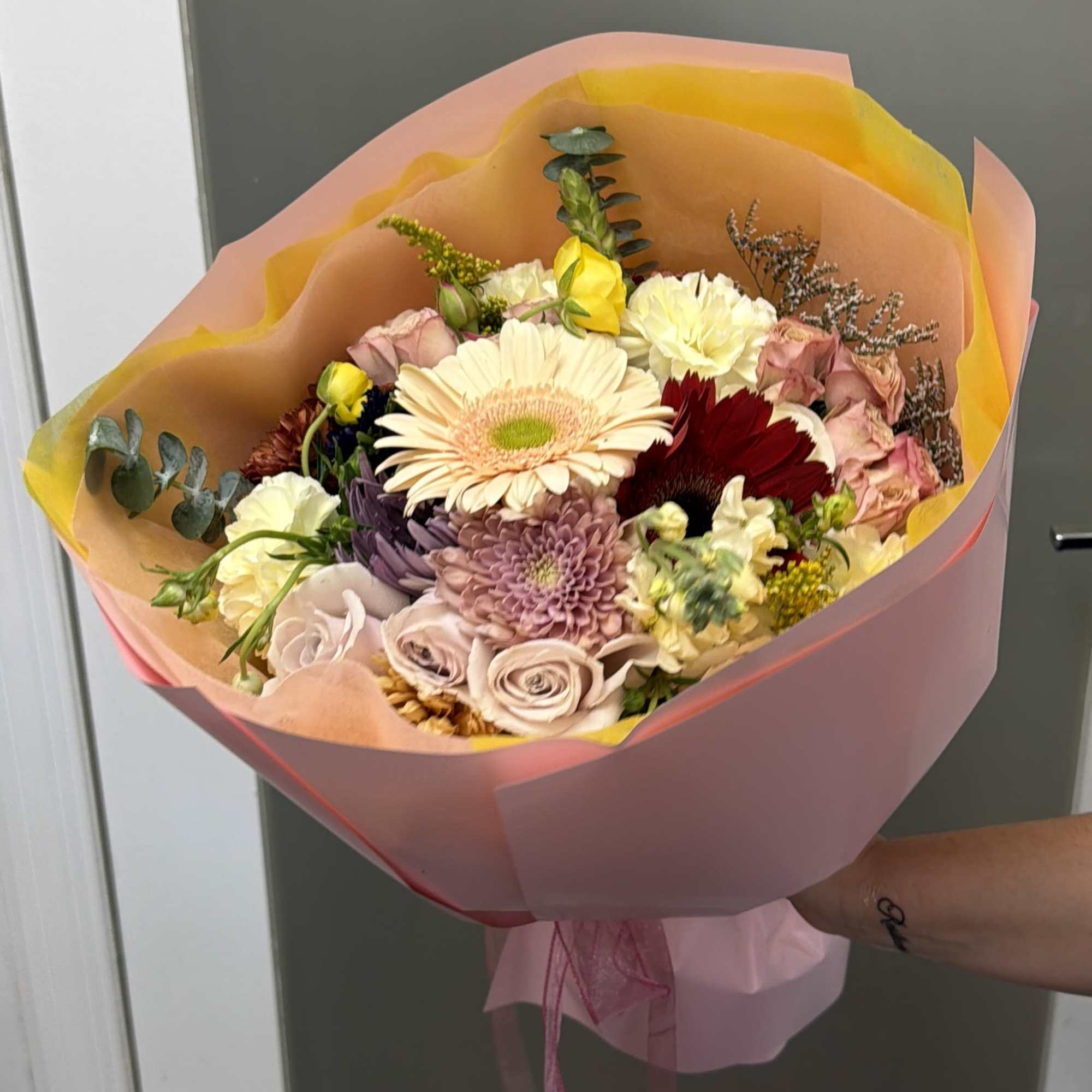 Hand-tied bouquet of mixed pastel flowers wrapped in pink and peach paper