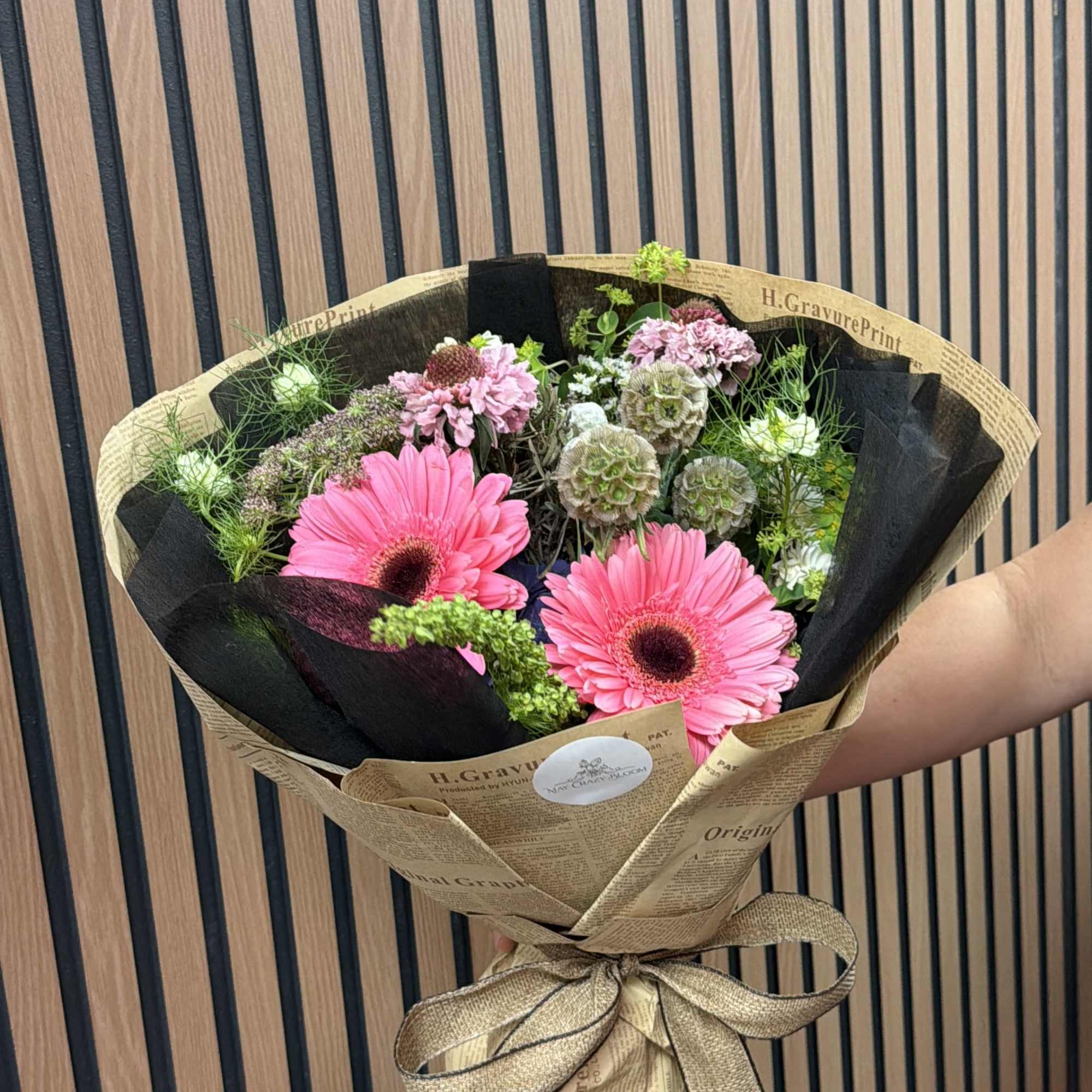 Pink gerbera daisy bouquet wrapped in brown paper with a ribbon