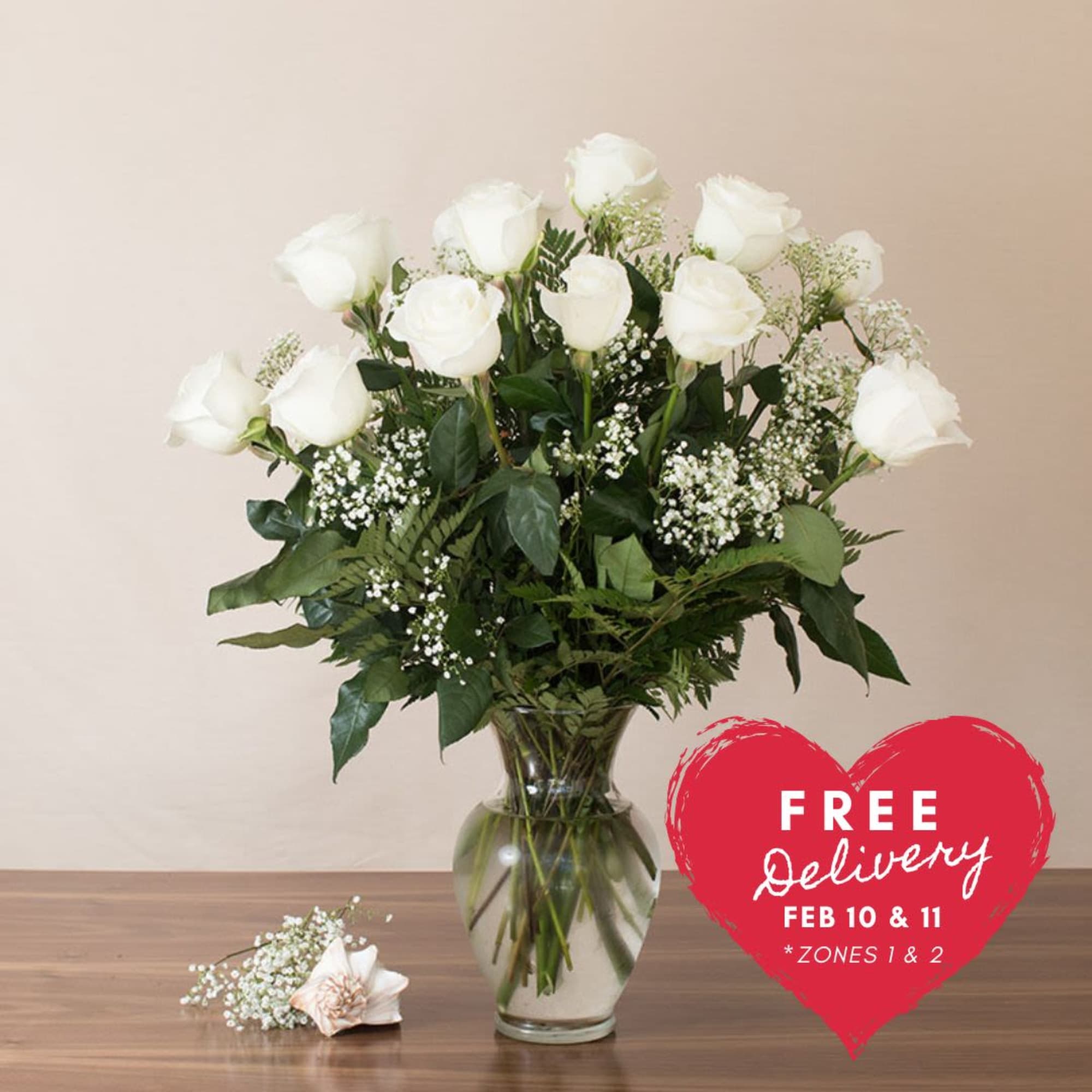 Tall arrangement of white roses with baby's breath in a clear glass vase on a wooden table