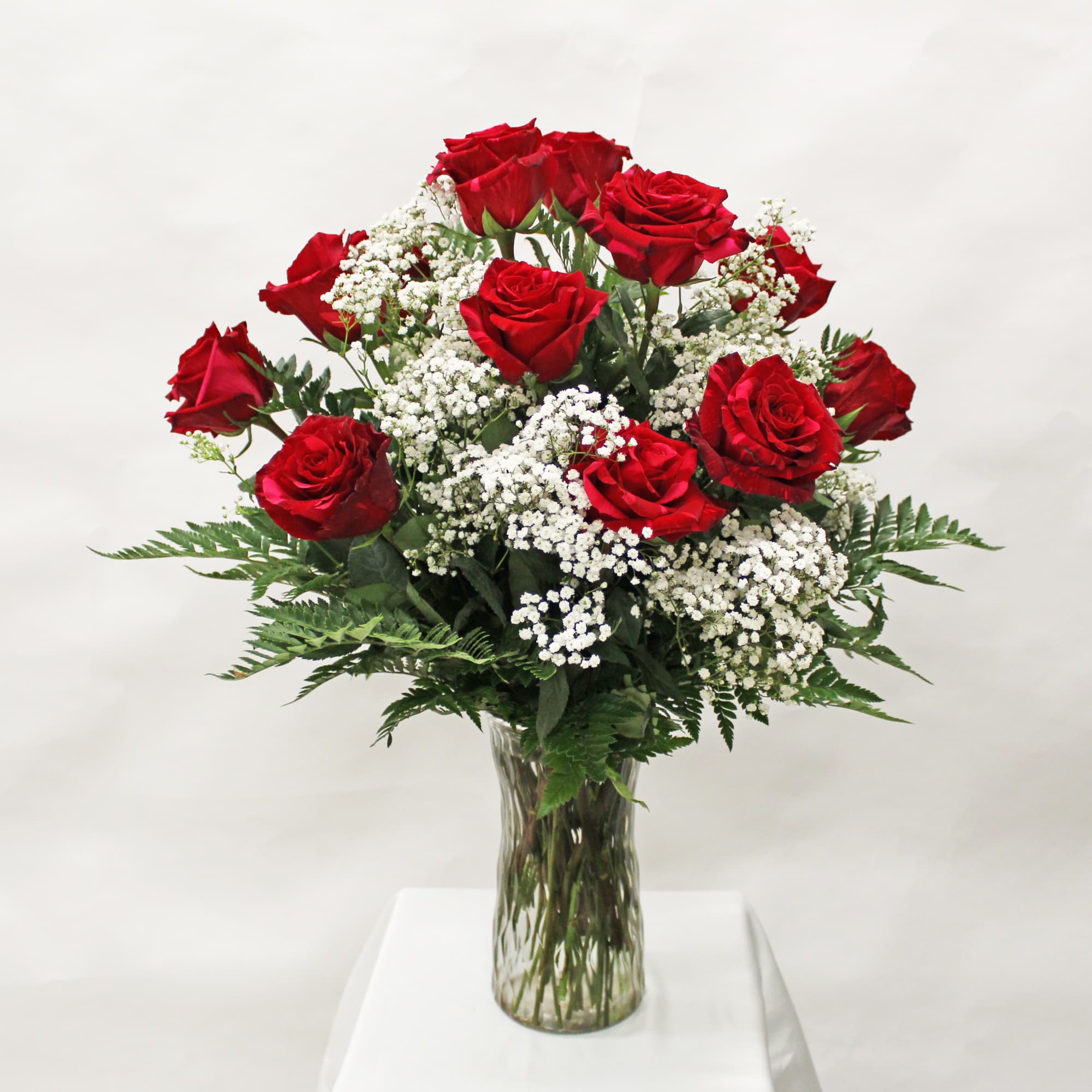 Tall arrangement of red roses and white filler flowers in a clear glass vase