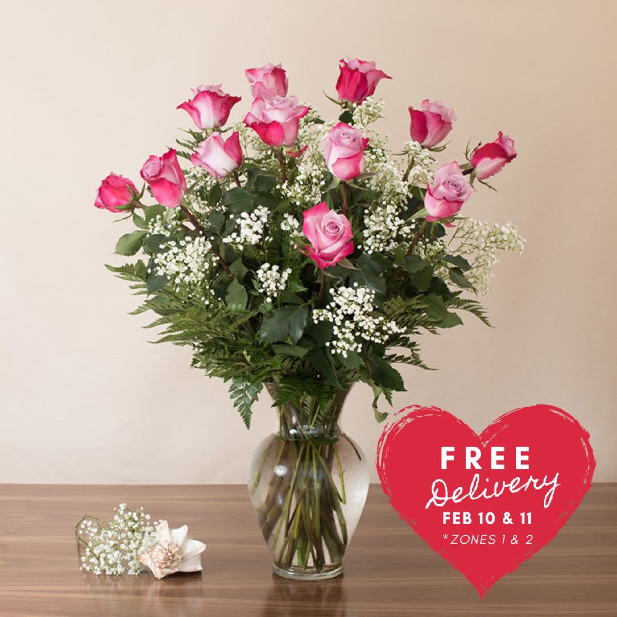 Tall arrangement of pink roses and white filler flowers in a clear glass vase