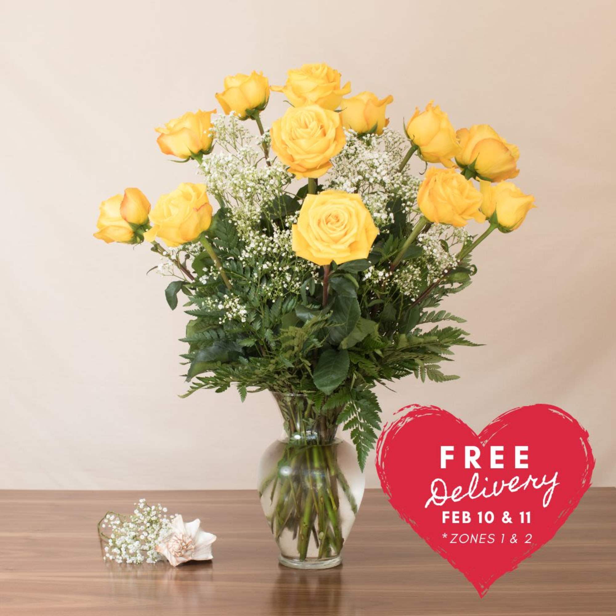 Tall arrangement of yellow roses and white filler flowers in a clear glass vase.