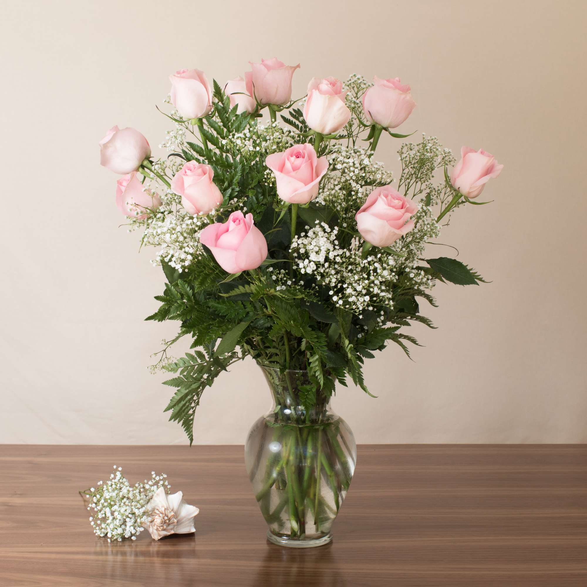 Tall bouquet of light pink roses and white filler flowers in a clear glass vase