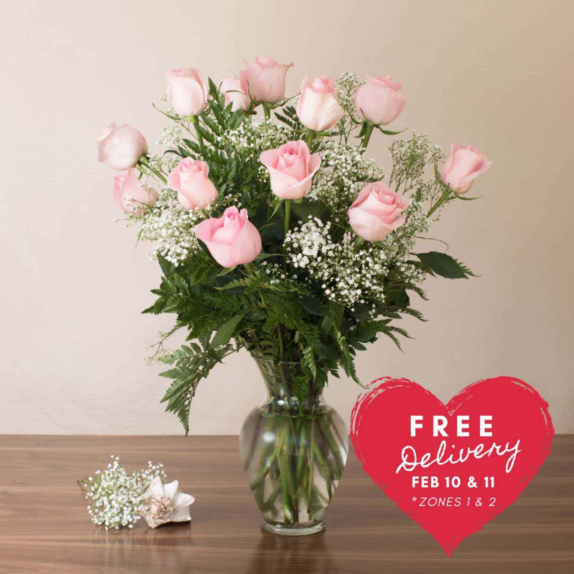 Clear glass vase of light pink roses with white filler flowers on a wooden table