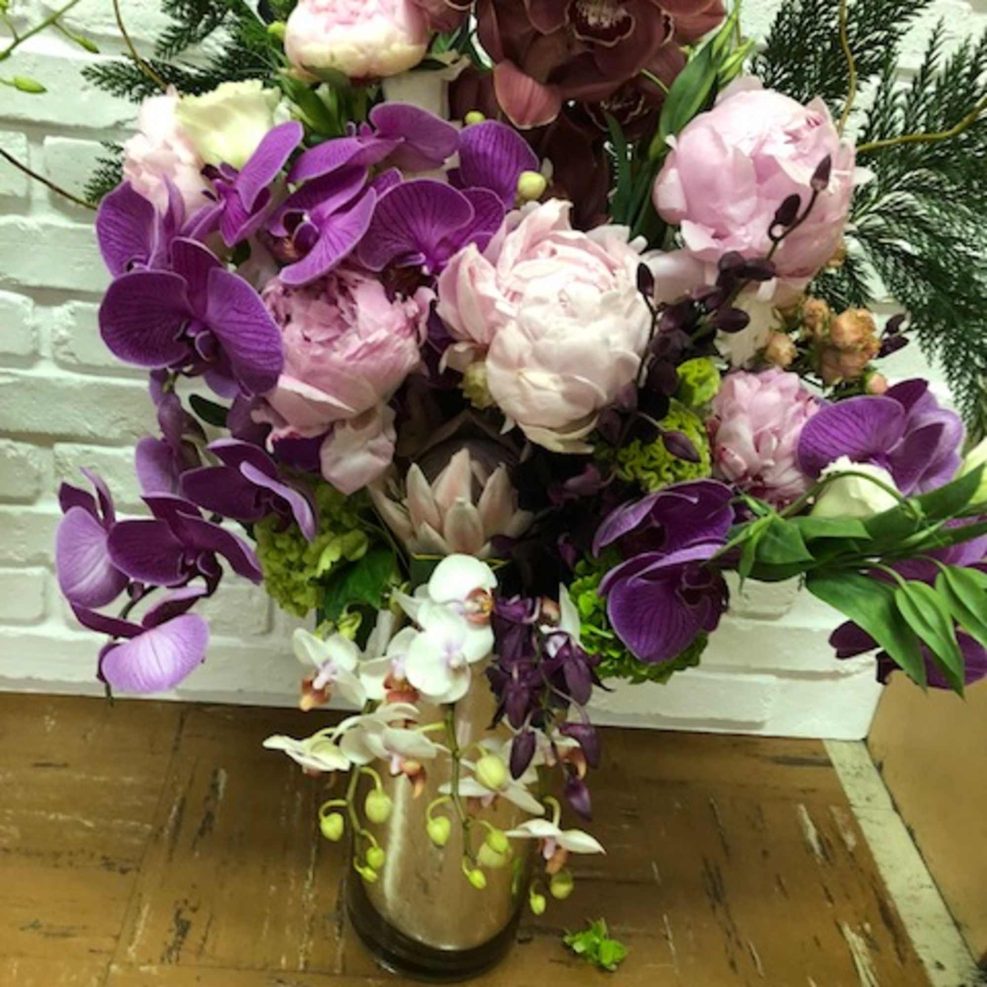 Tall arrangement of purple and pink orchids with peonies in a vase