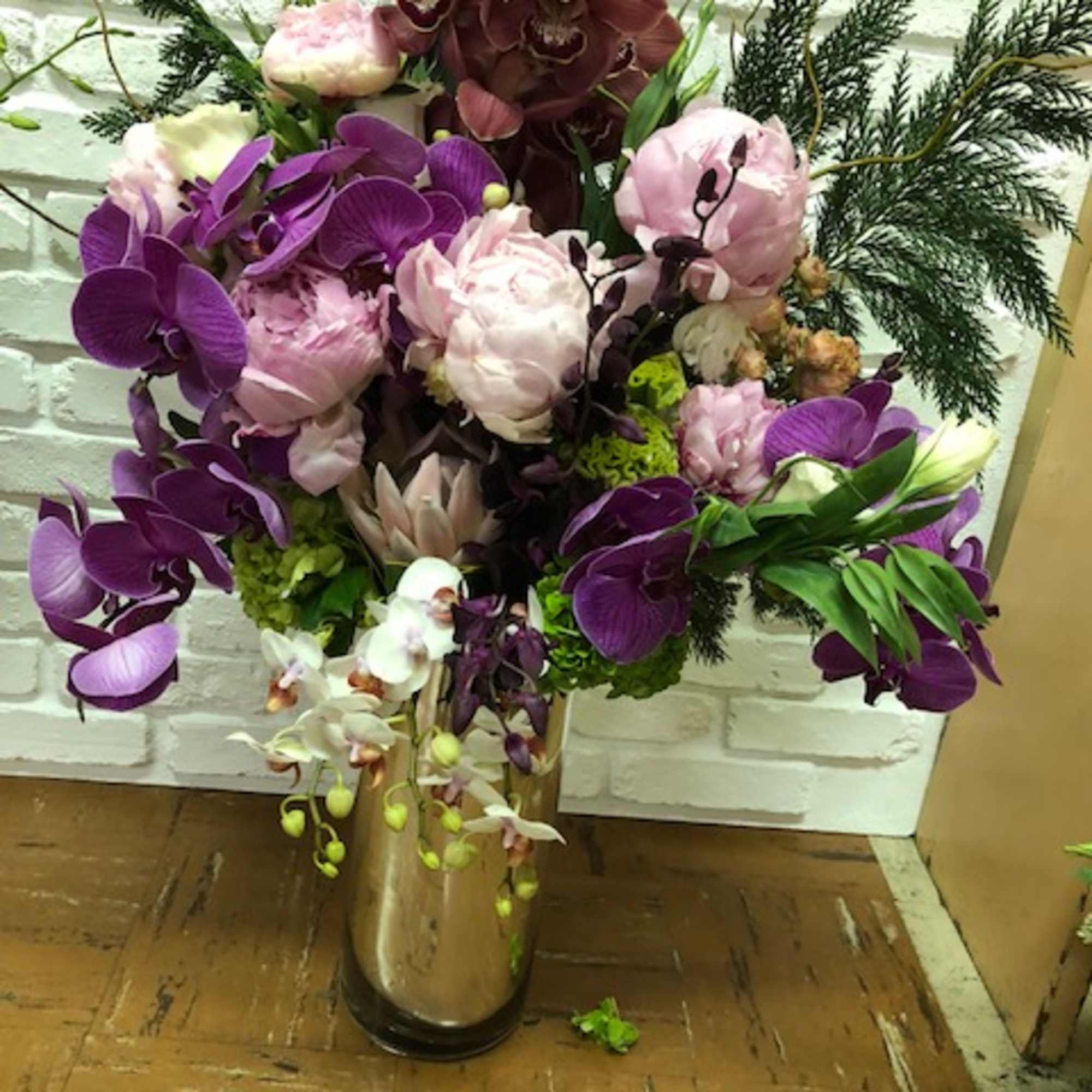 Peony and orchid focused designer medley presented in a tall clear glass