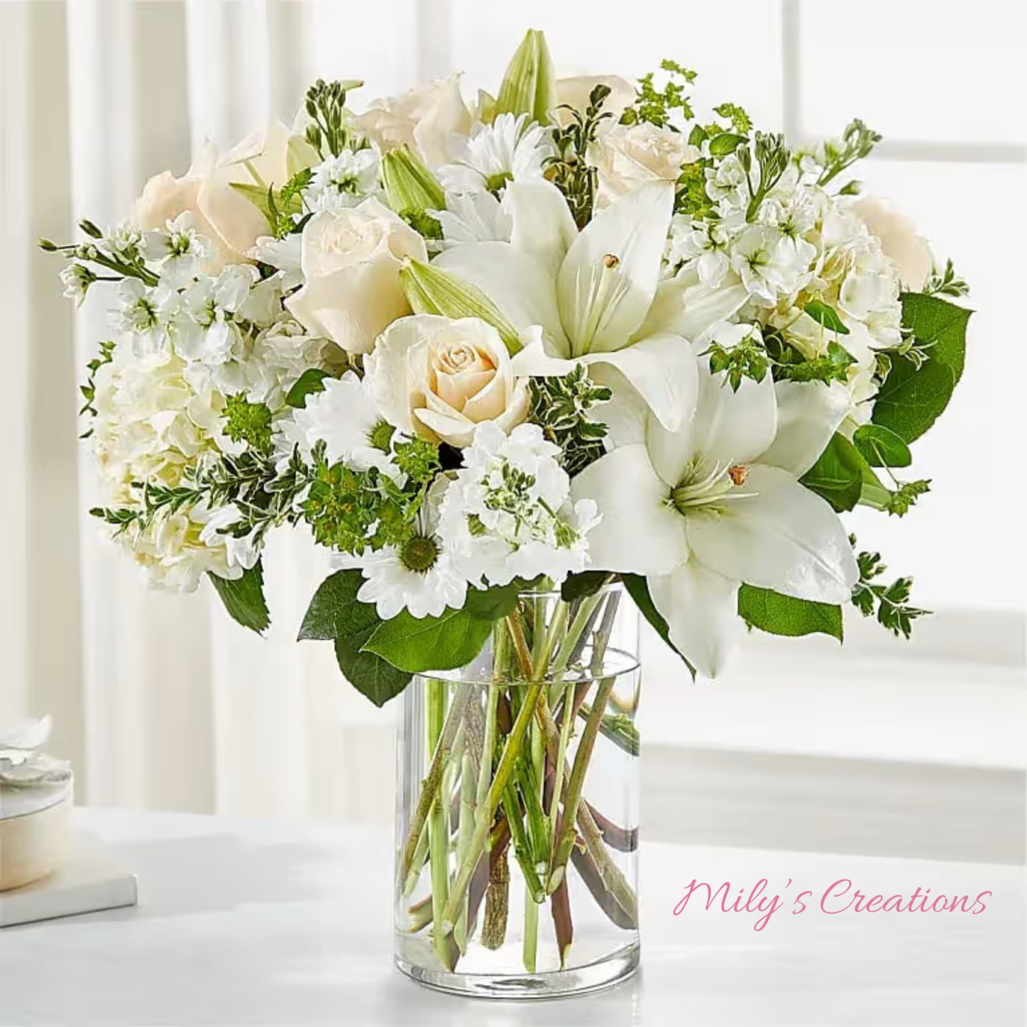 White lilies, cream roses, and daisies arranged in a clear glass vase