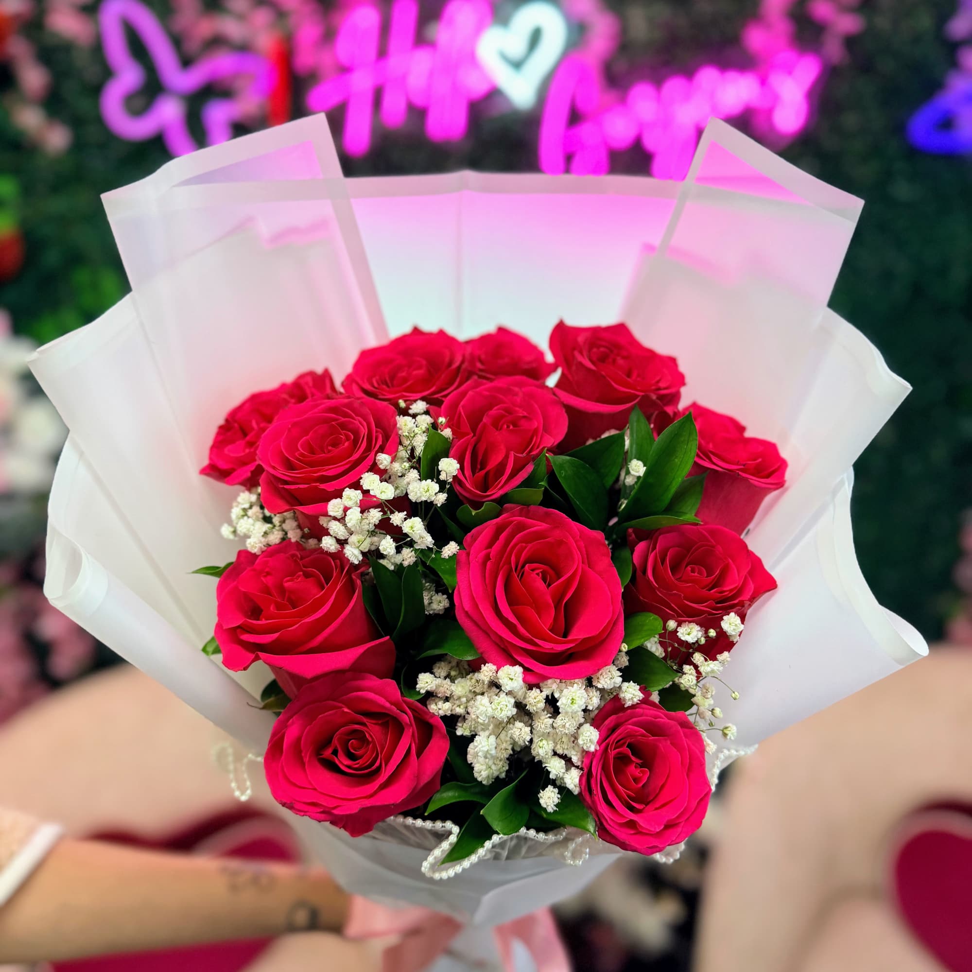 Bouquet of hot pink roses with white filler flowers wrapped in white paper and pink ribbon