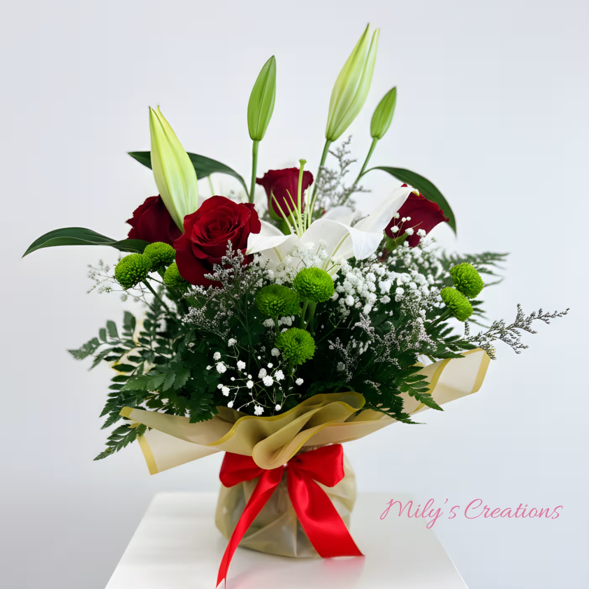 Mixed arrangement of red roses, white lilies, and green button poms wrapped with gold paper and red ribbon
