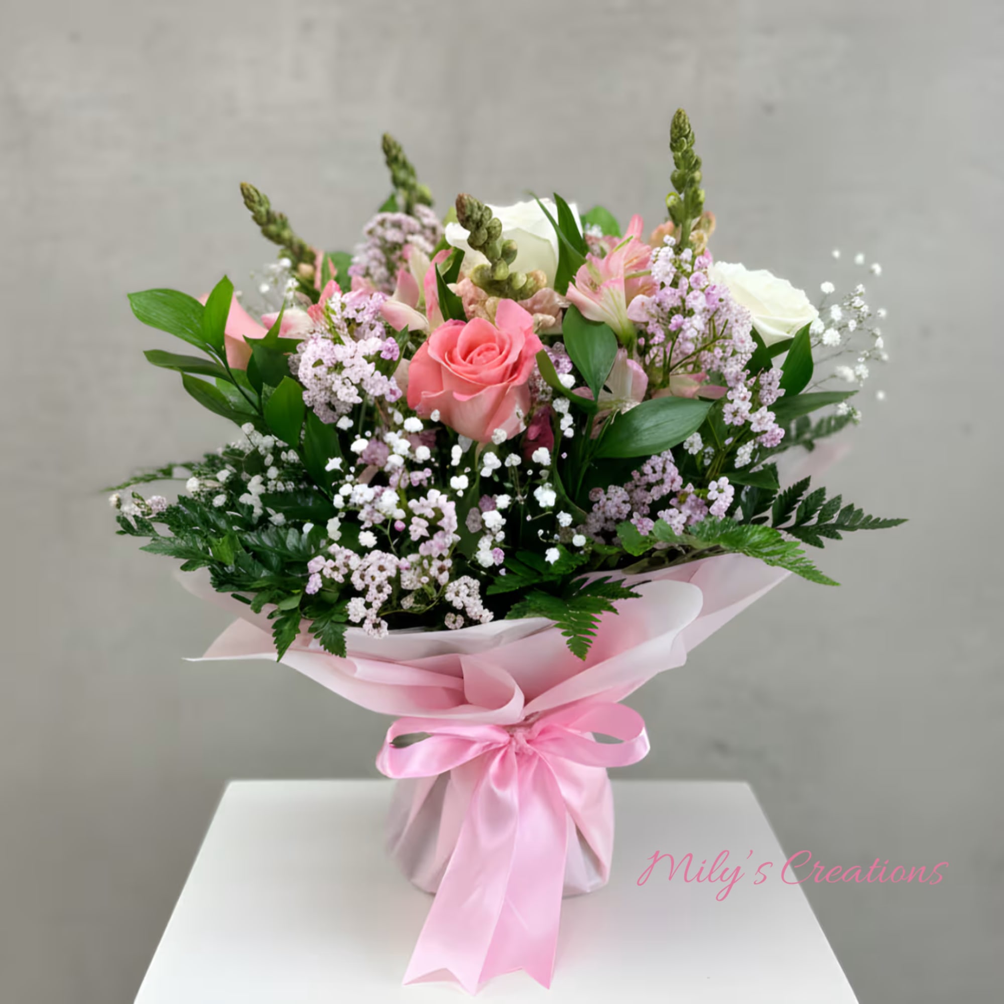 Hand-tied bouquet of pink roses and mixed pastel flowers wrapped in pink paper with a satin bow.