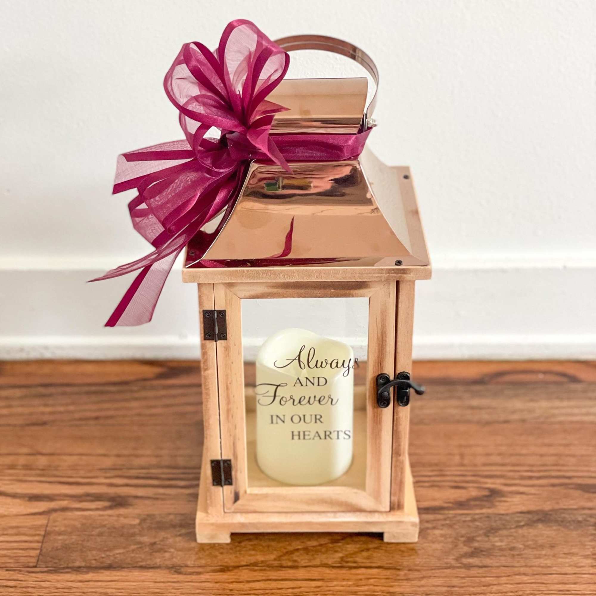 Wooden lantern with white memorial candle and burgundy ribbon bow on the handle.