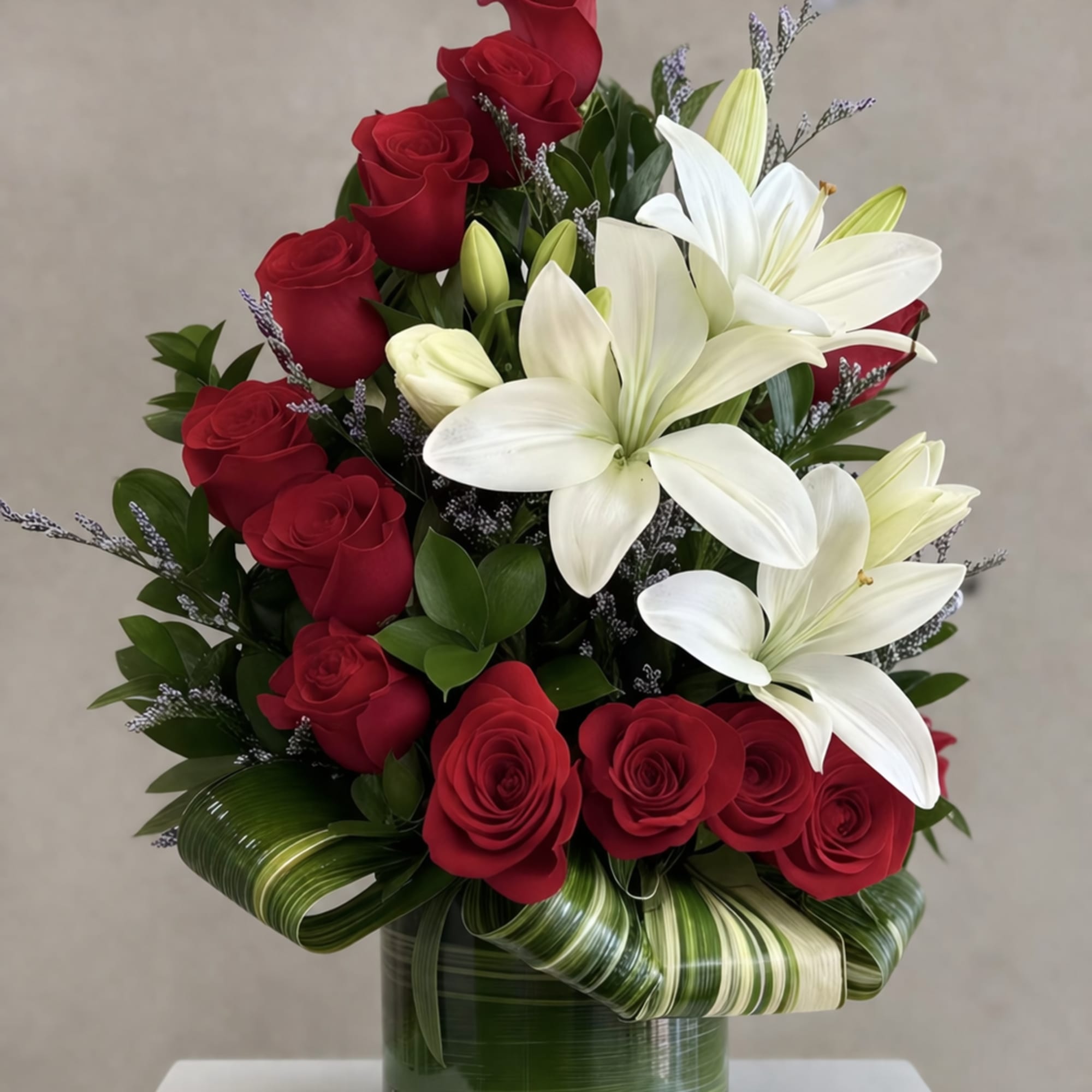 Arrangement of red roses and white lilies in a clear vase with decorative green leaves.