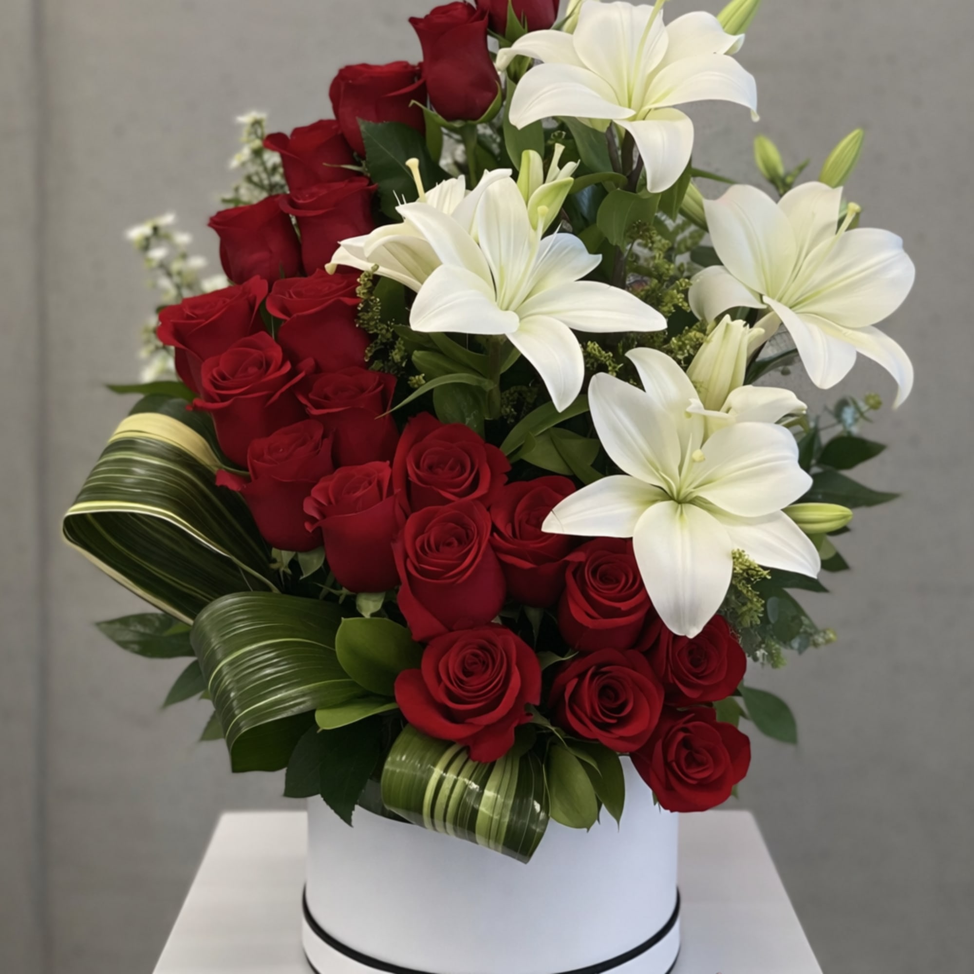 Red roses and white lilies in a white hatbox with decorative looped green leaves