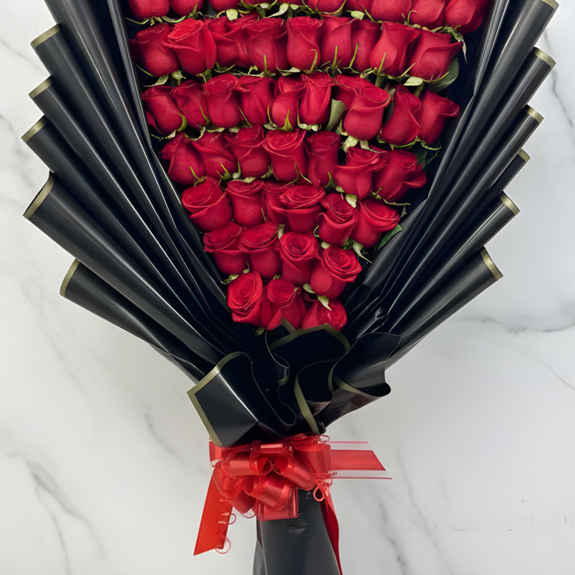 Large bouquet of tightly packed red roses wrapped in black fan-shaped paper with a red ribbon bow.