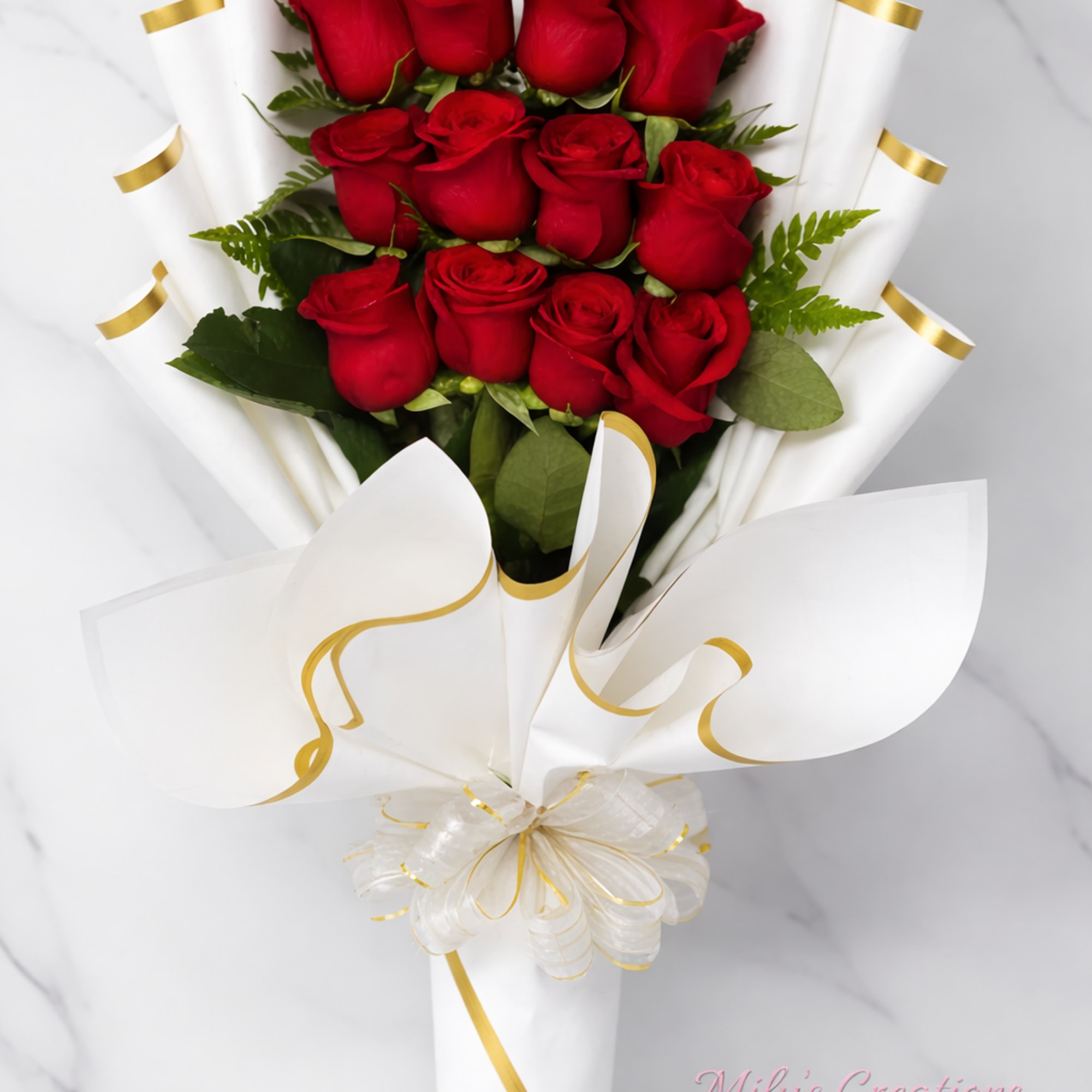 Hand-tied bouquet of red roses wrapped in white paper with gold trim and a decorative bow.