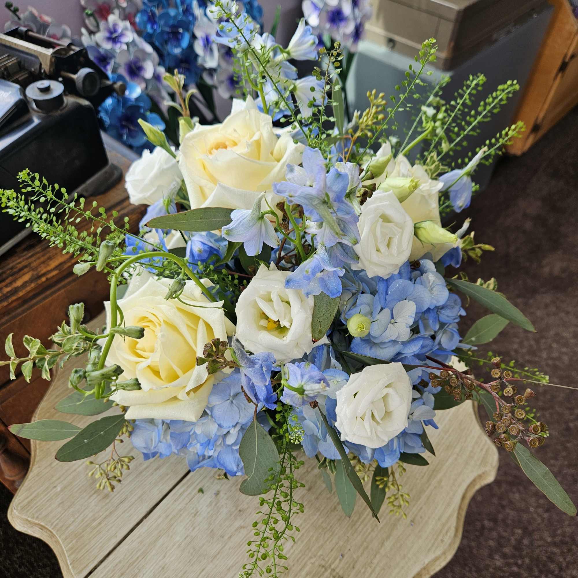Low arrangement of pale yellow roses, white lisianthus, and blue hydrangeas on a small table