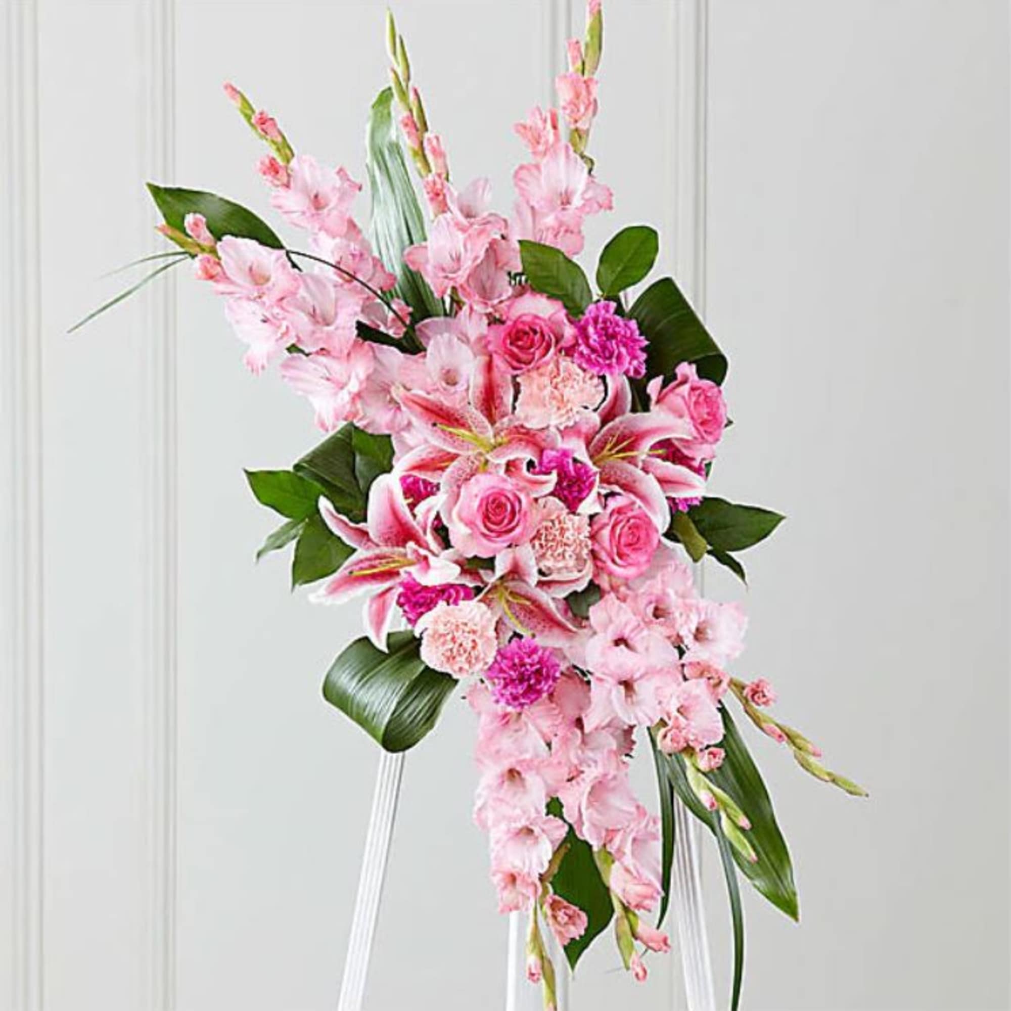 Tall pink standing spray with lilies, roses, and gladiolus on a white easel.