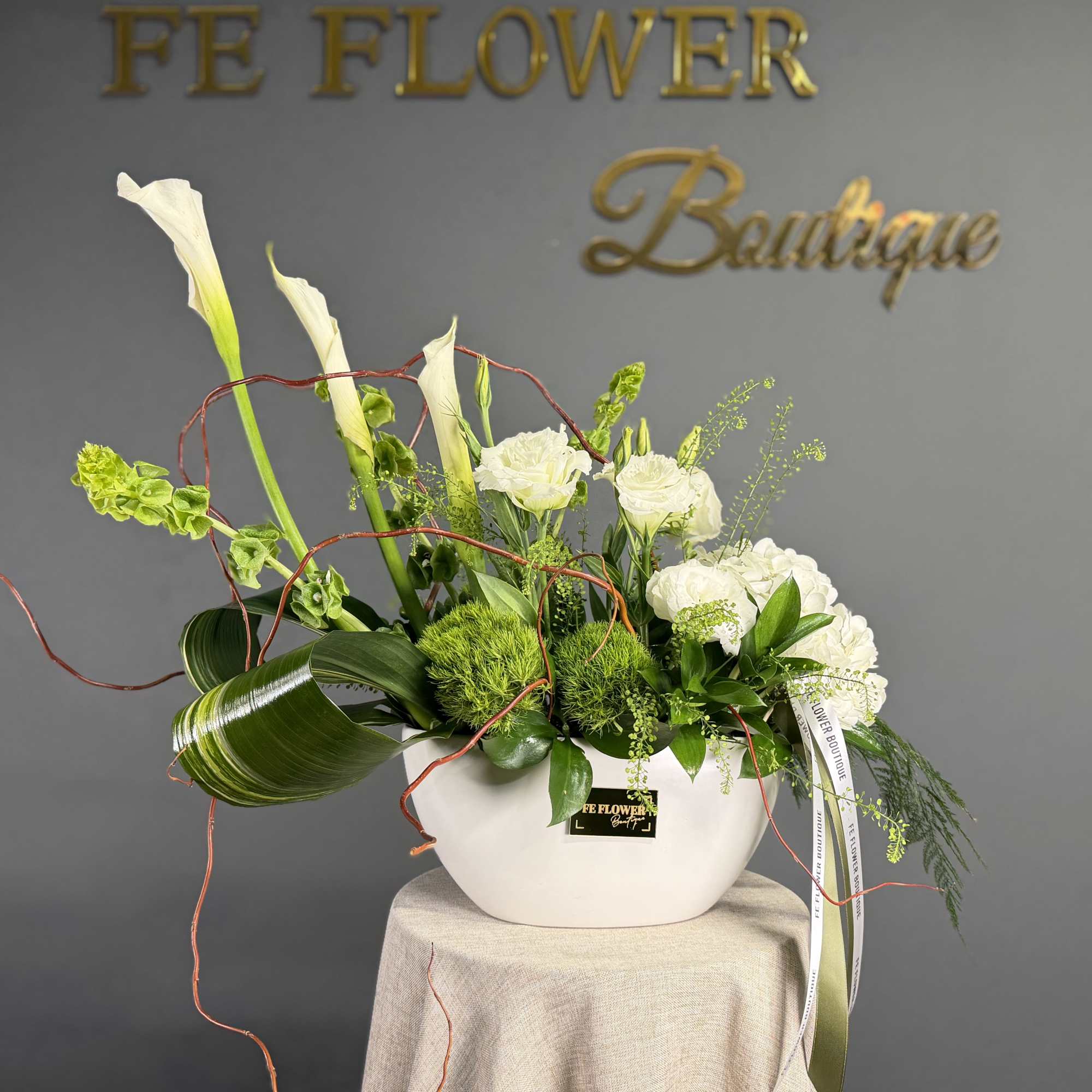 Modern white and green floral arrangement with calla lilies and roses in a low white ceramic bowl