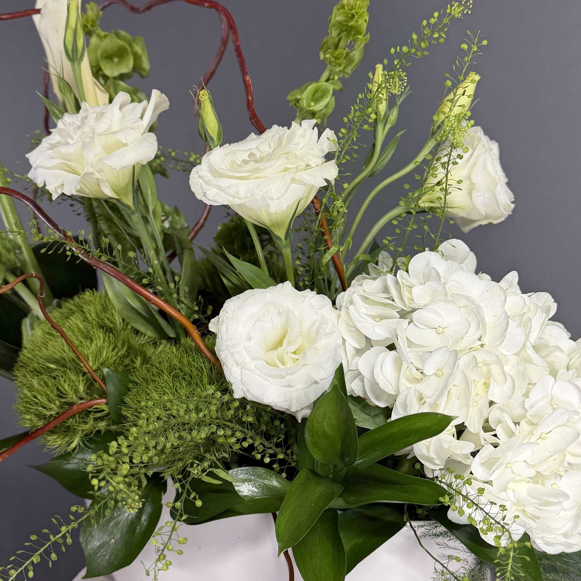 Asymmetrical white and green floral arrangement with hydrangeas and lisianthus in a white bowl.