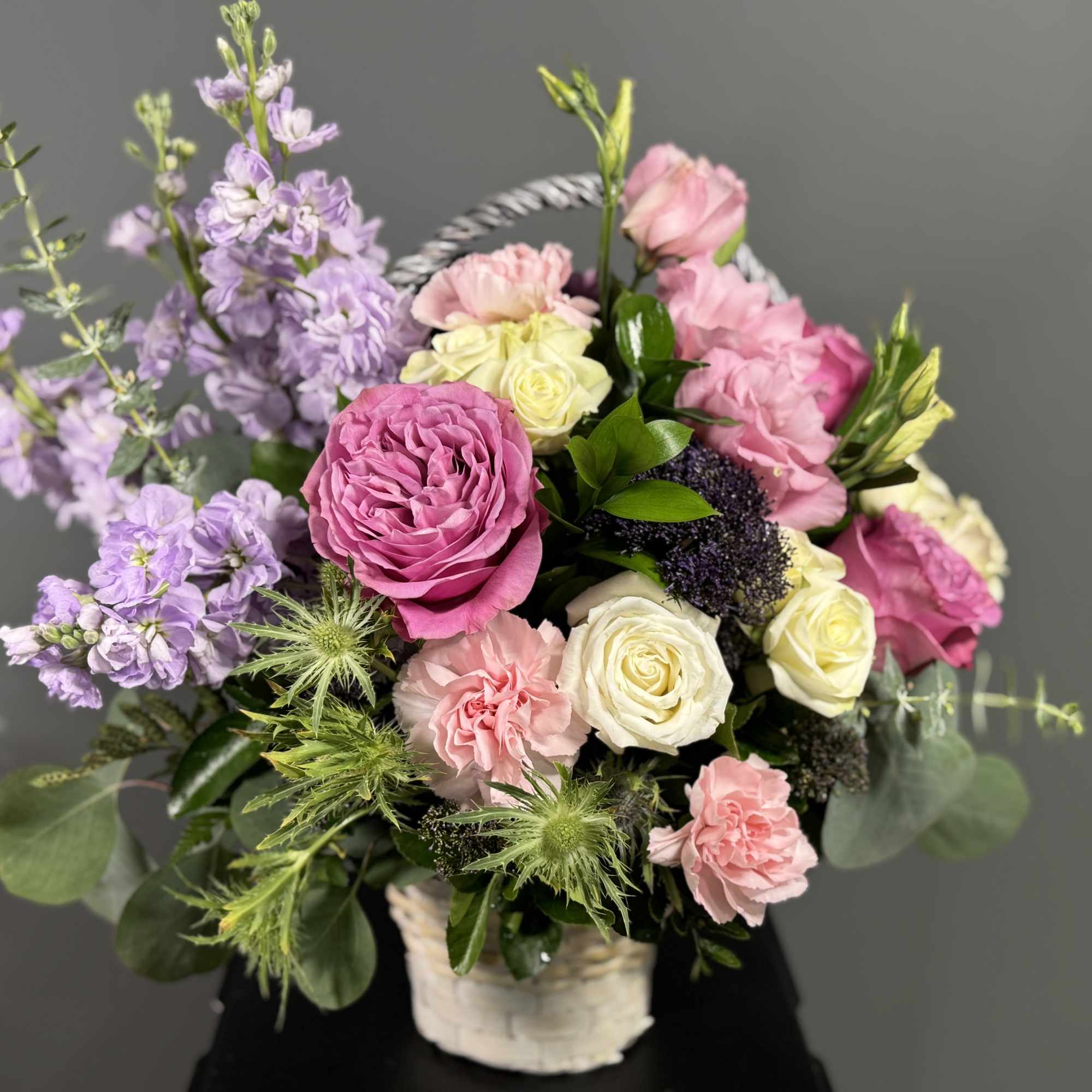 Basket arrangement of pink, cream, and lavender flowers in a white wicker container