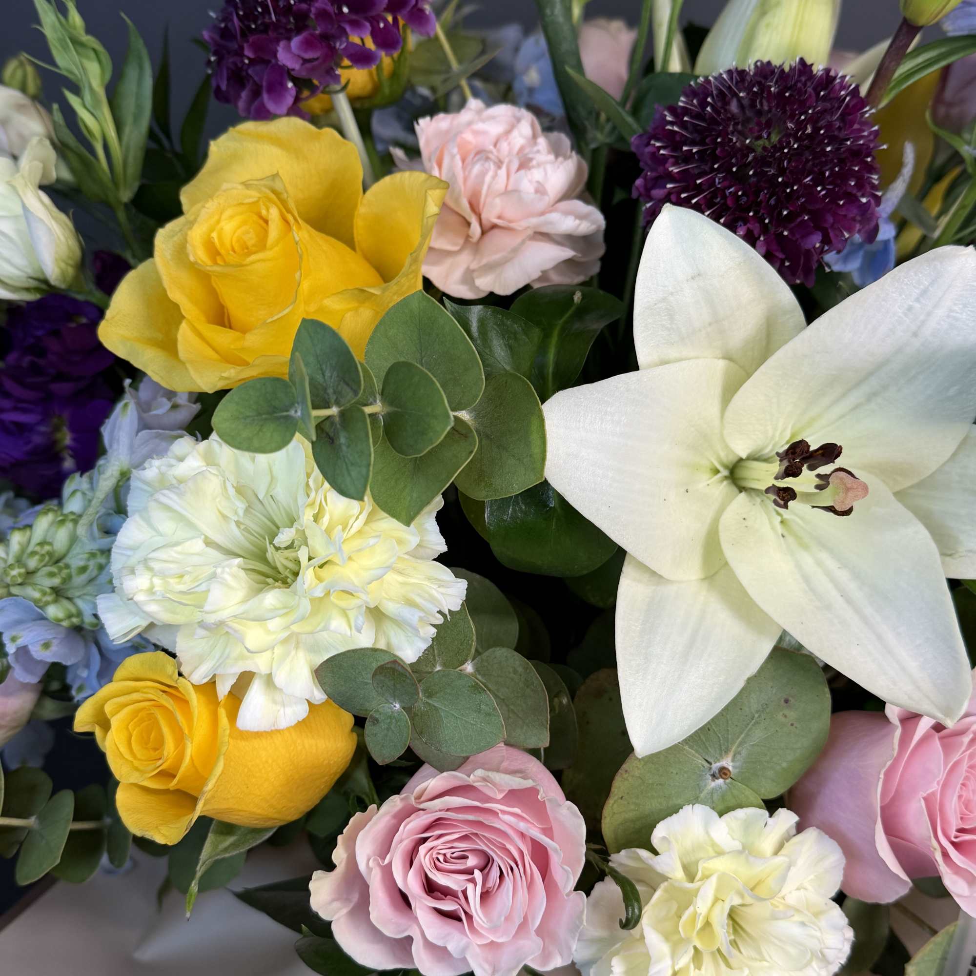 Colorful mixed bouquet with yellow roses, pink roses, white lily, and pale carnations.