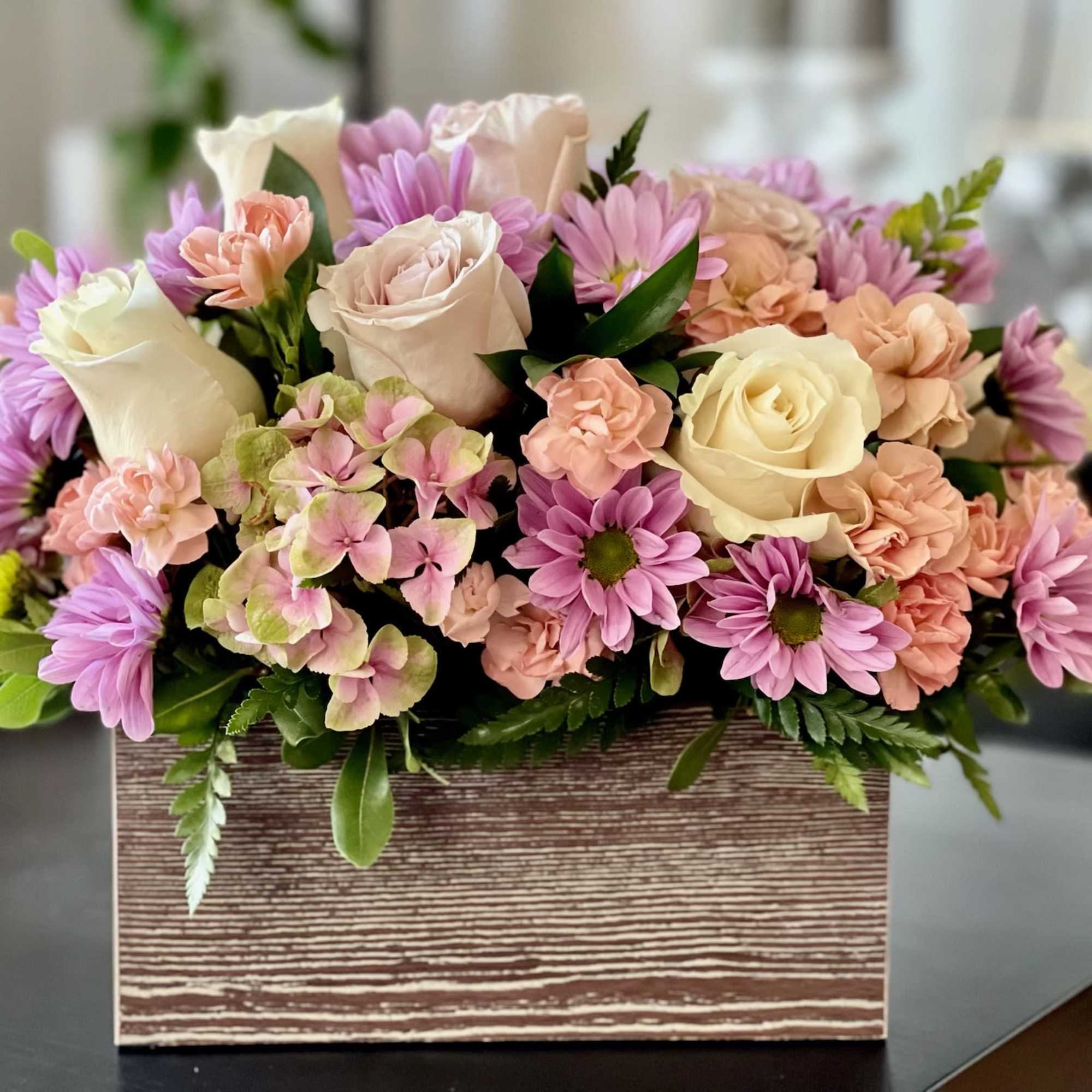 Pastel roses, daisies, carnations, and hydrangea arranged in a rustic wooden box