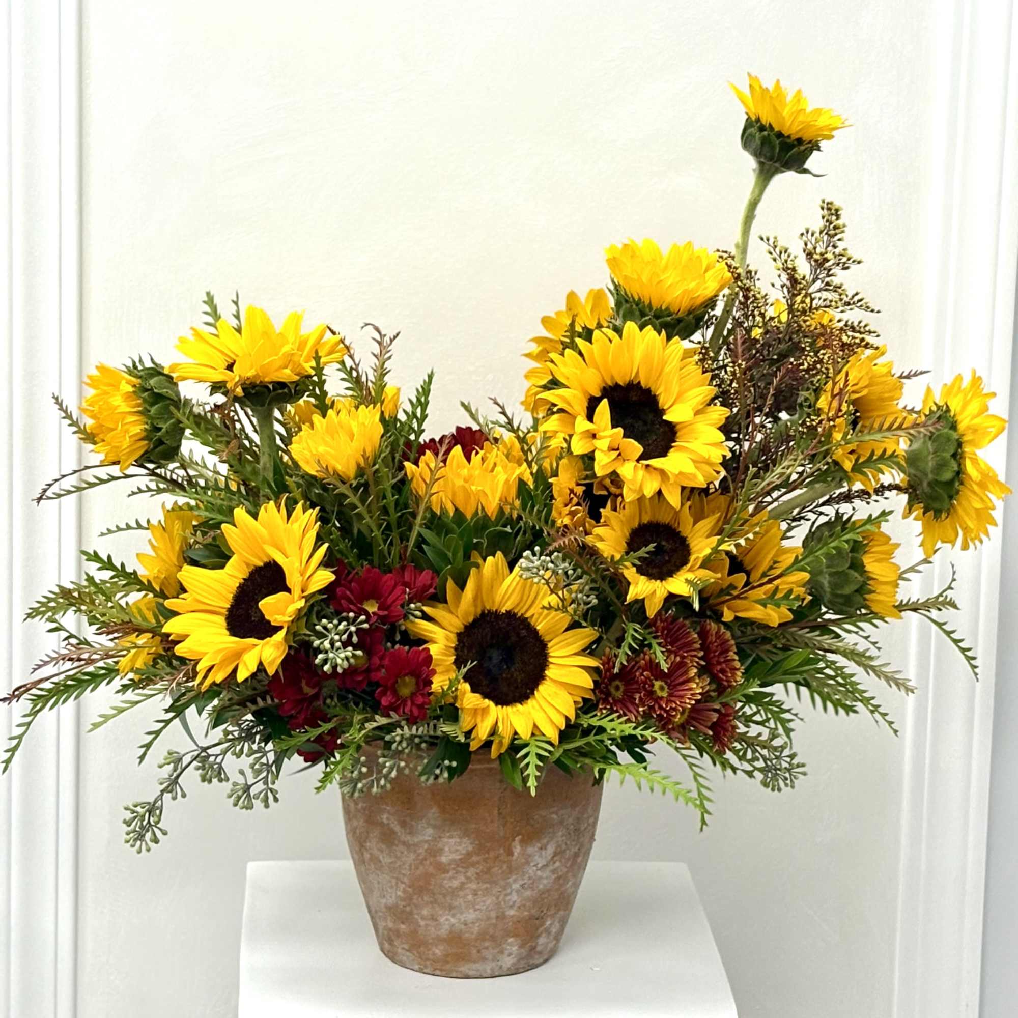 Arrangement of yellow sunflowers and red chrysanthemums in a rustic clay pot
