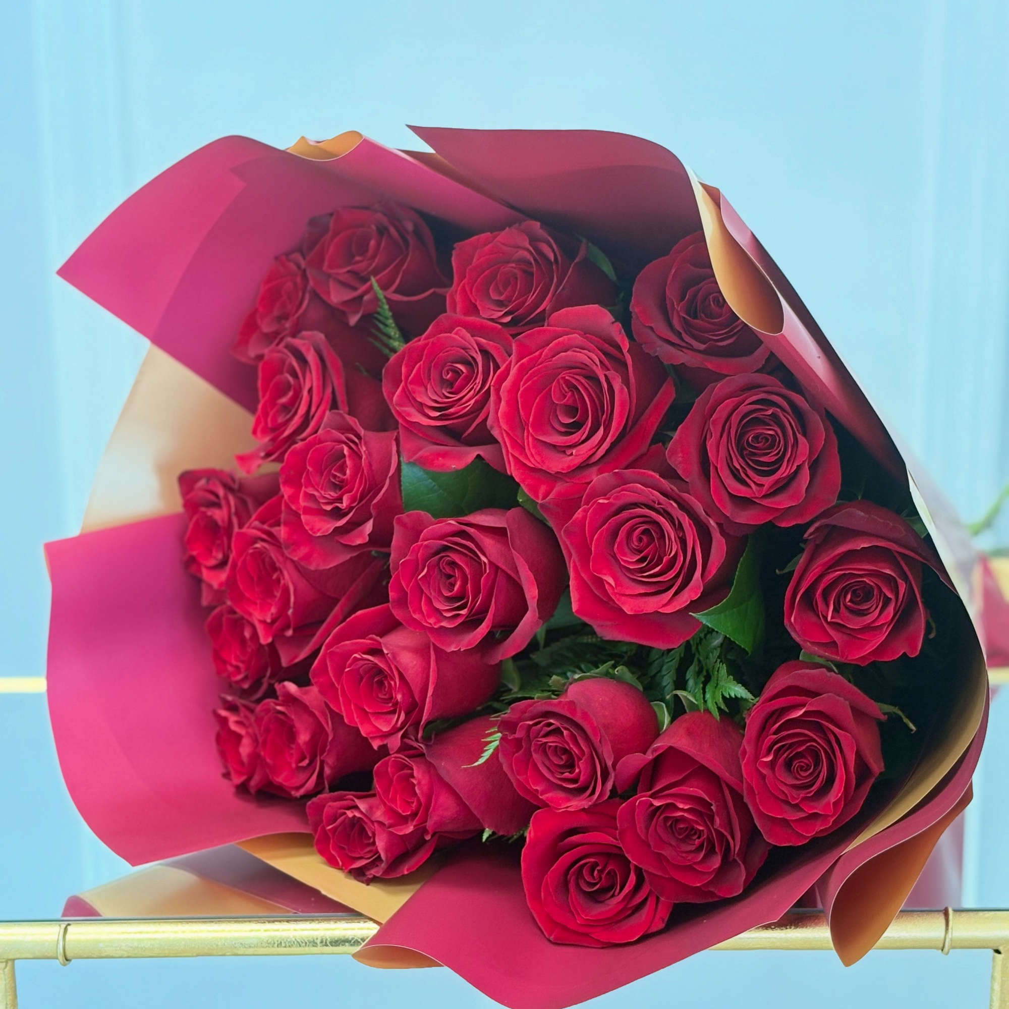 Large bouquet of red roses wrapped in pink and peach paper against a light blue background