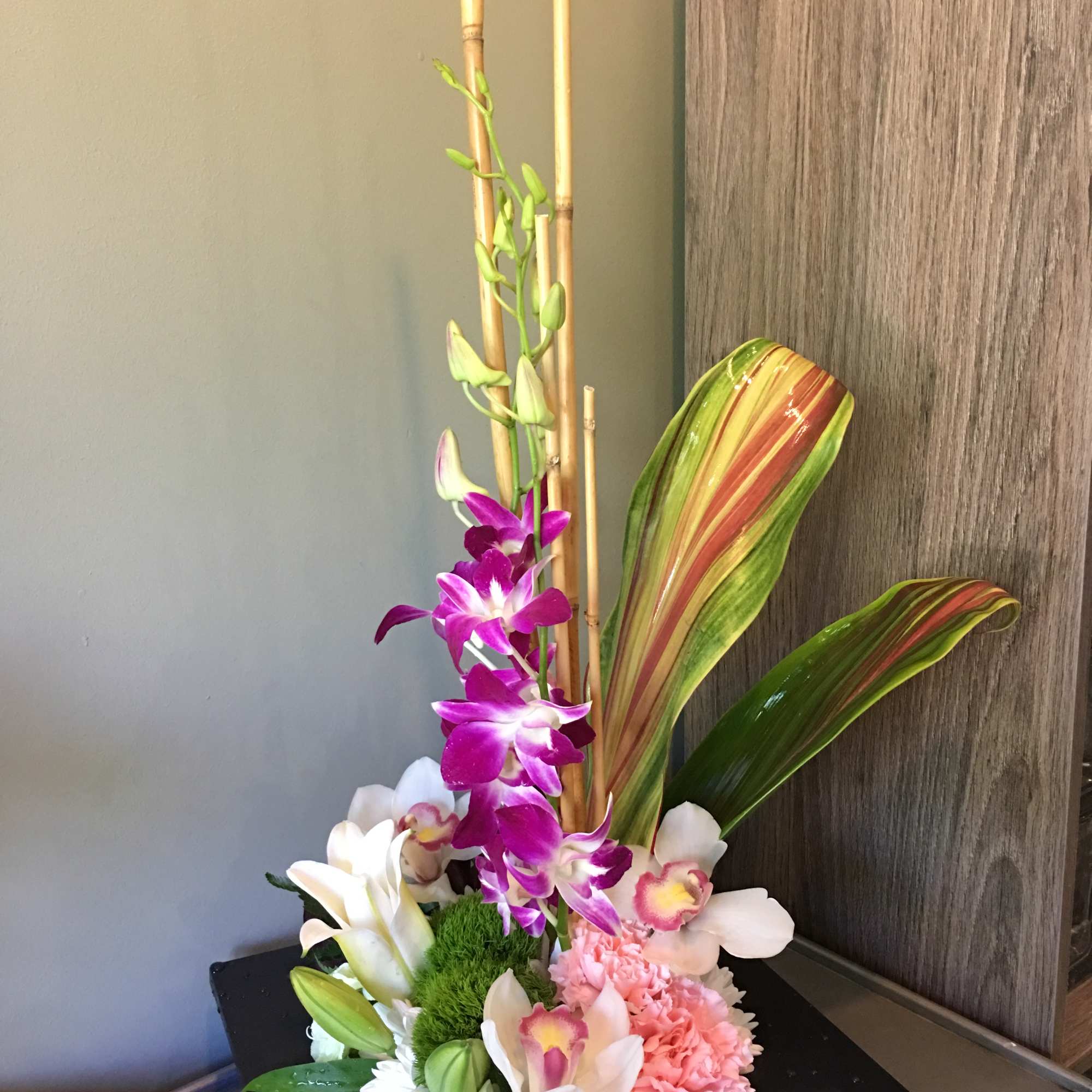 Modern arrangement with purple orchids, white lilies, pink carnations and bamboo in a low black container