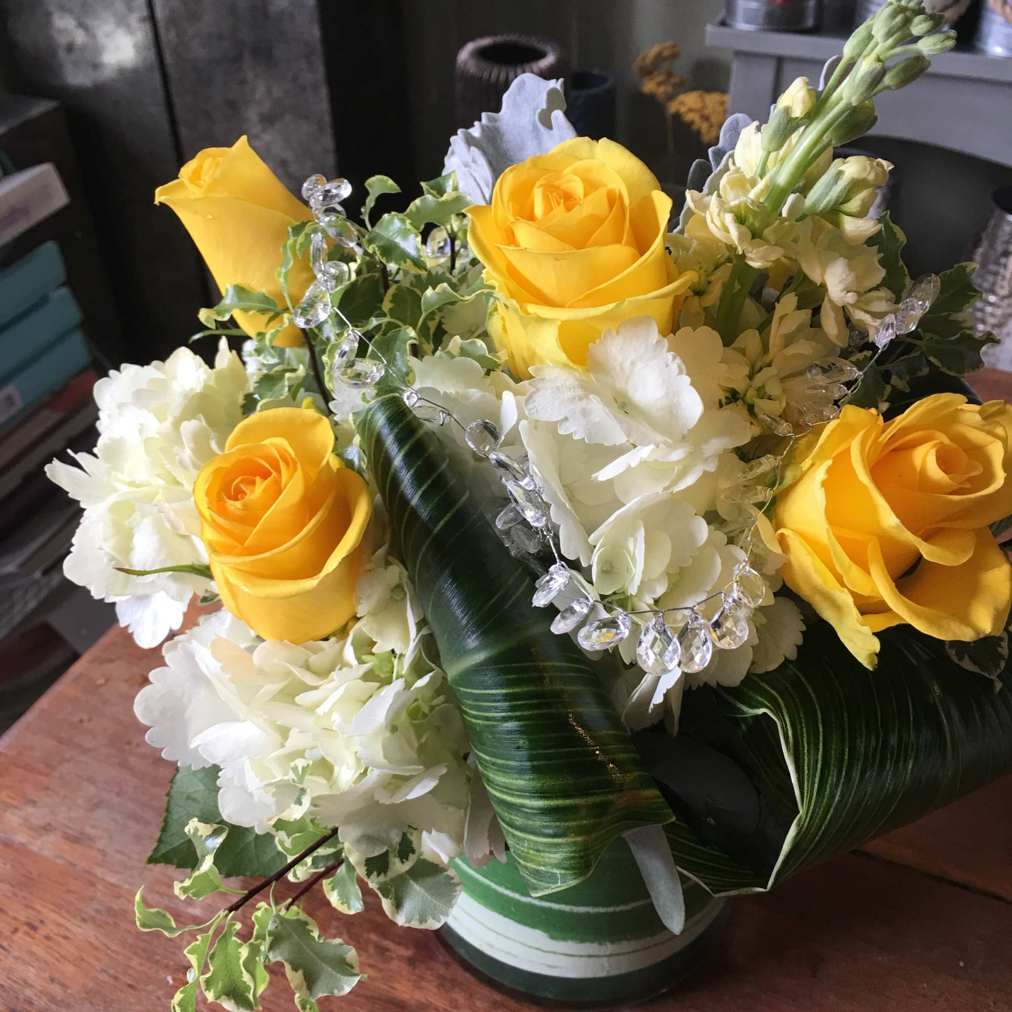 Low arrangement of yellow roses and white hydrangeas with folded green leaves in a green vase