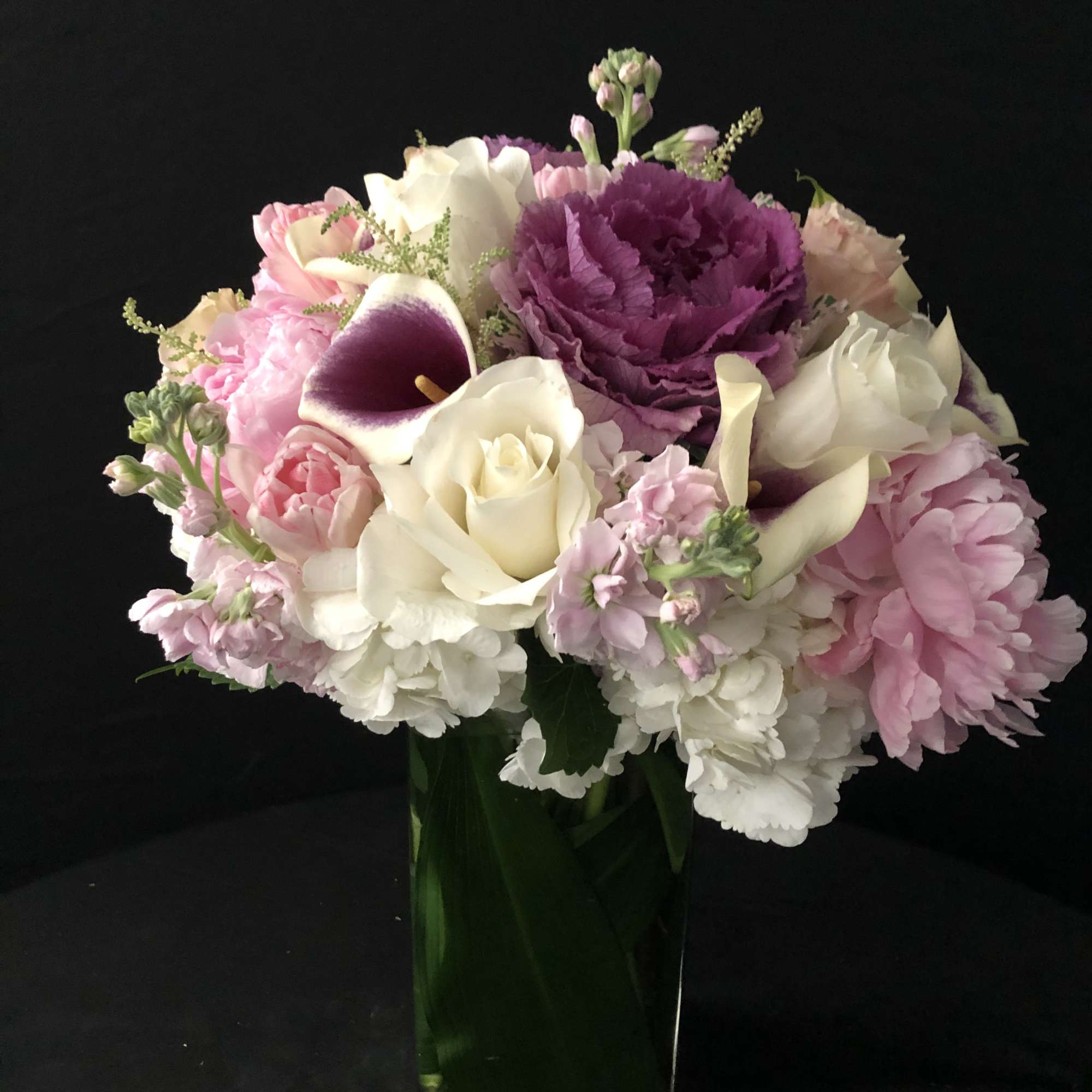 Pink, white, and purple flower arrangement with roses and calla lilies in a tall rectangular glass vase