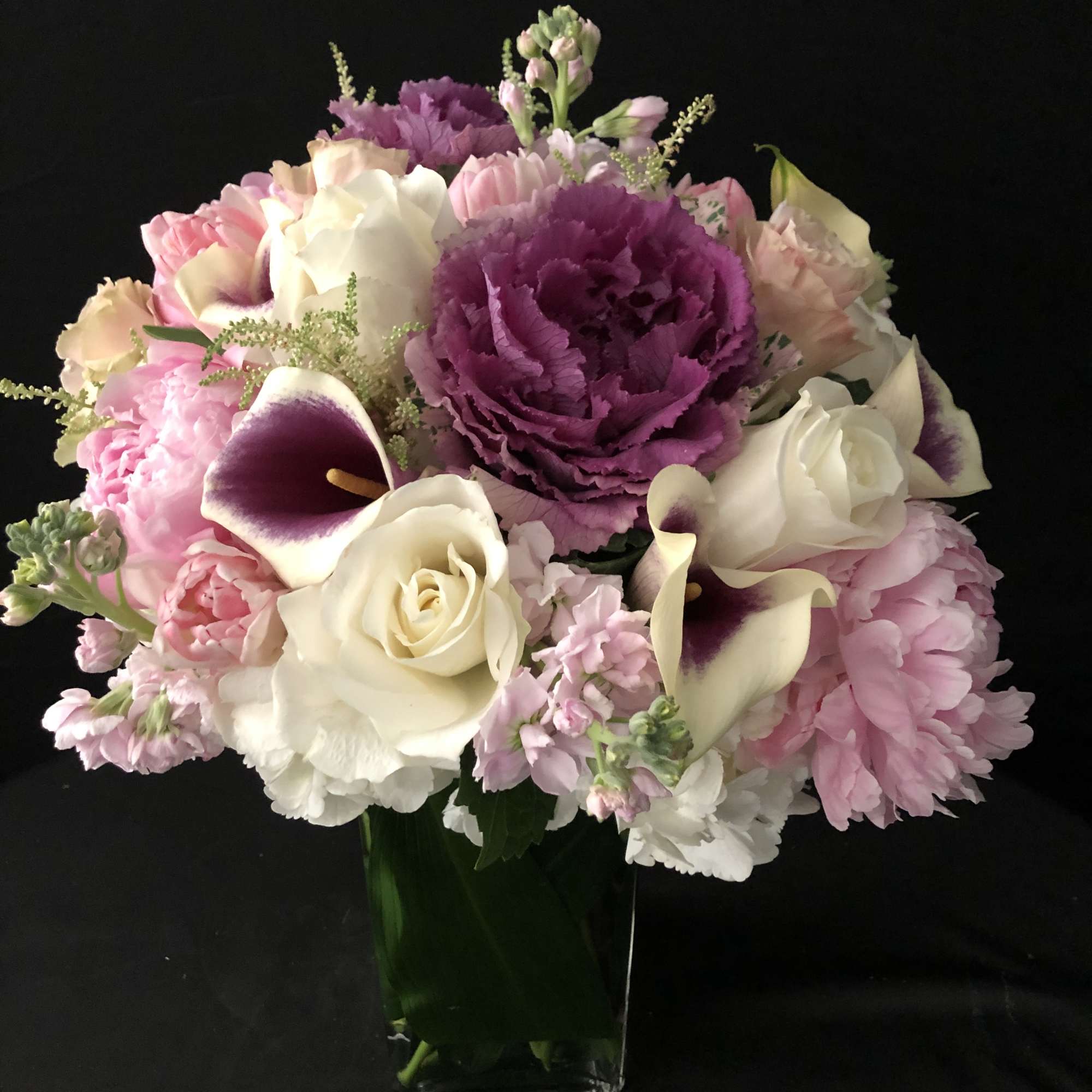Round arrangement of pink peonies, white roses, and purple blooms in a clear glass vase