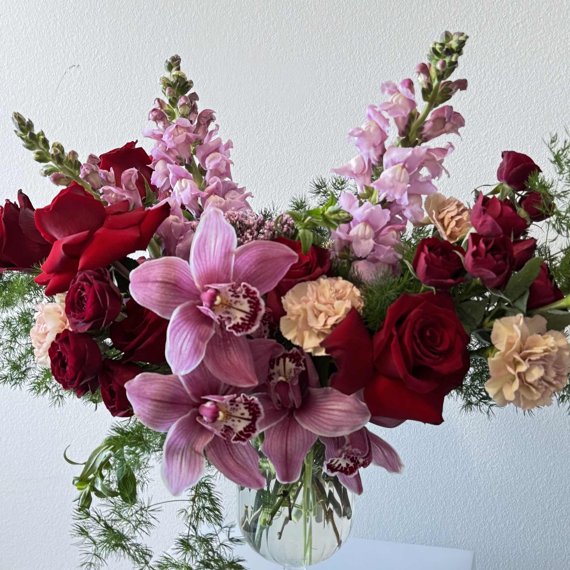 Bouquet of red roses, pink orchids, and peach carnations in a glass vase