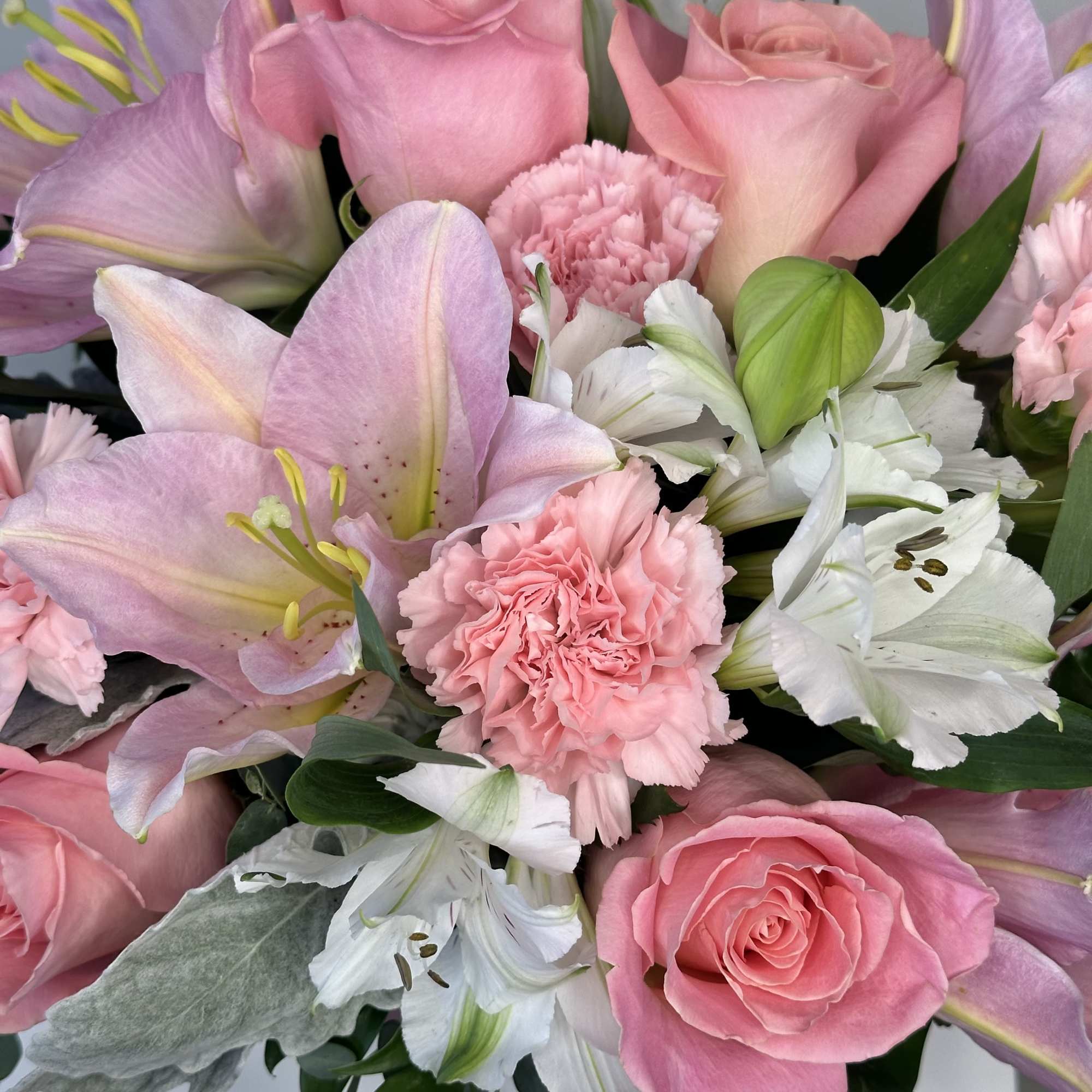 Arrangement of pink roses, lilies, and carnations with white alstroemeria in a compact design