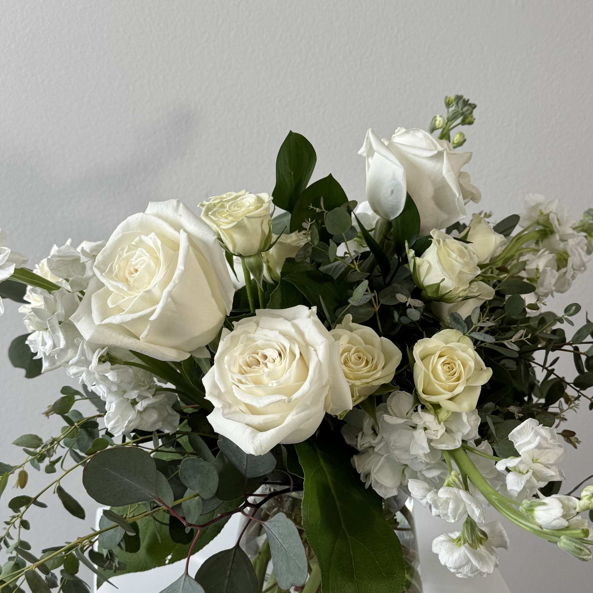 White roses arranged in a clear glass vase with greenery