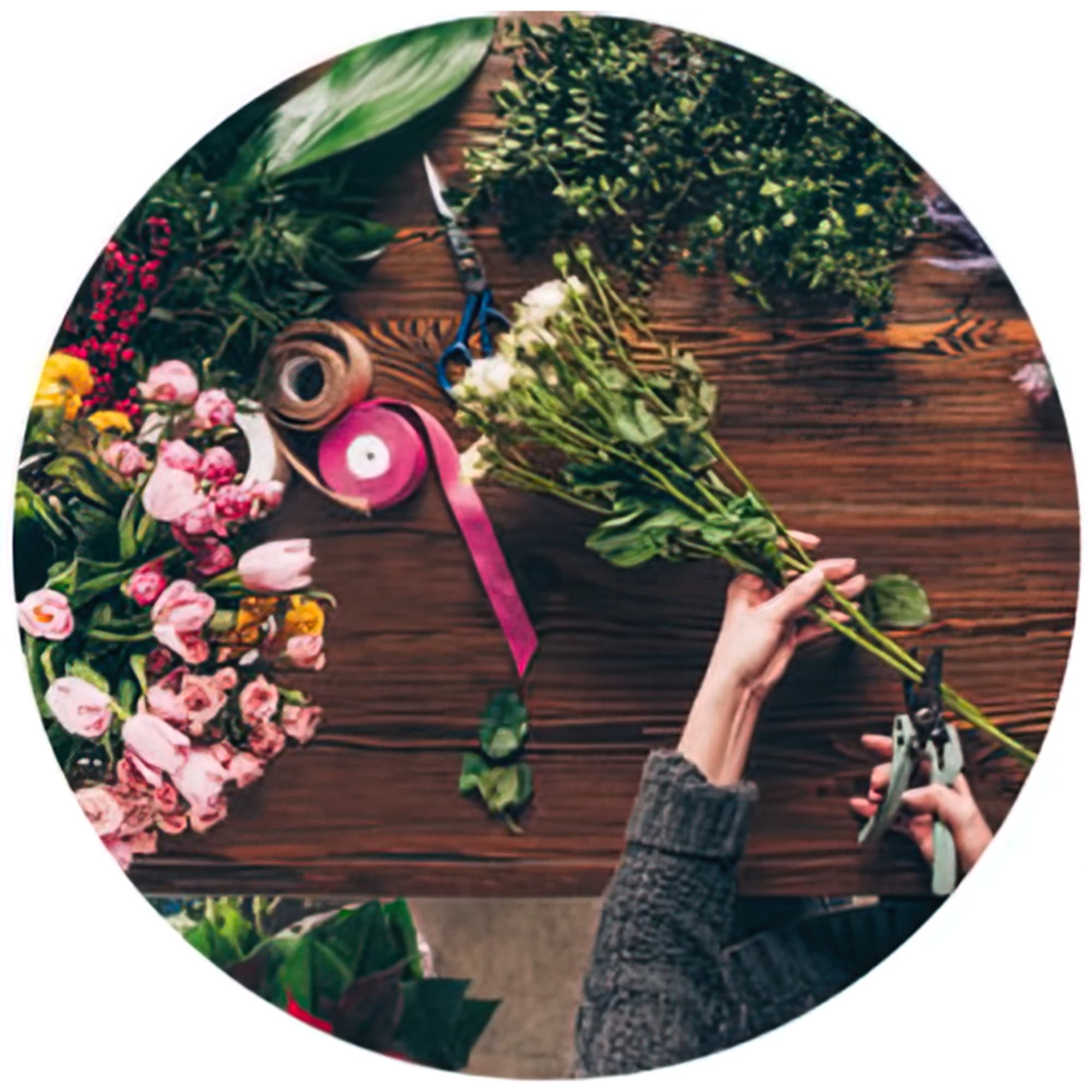 Florist hands arranging a mixed bouquet on a wooden table with pink flowers and ribbon.
