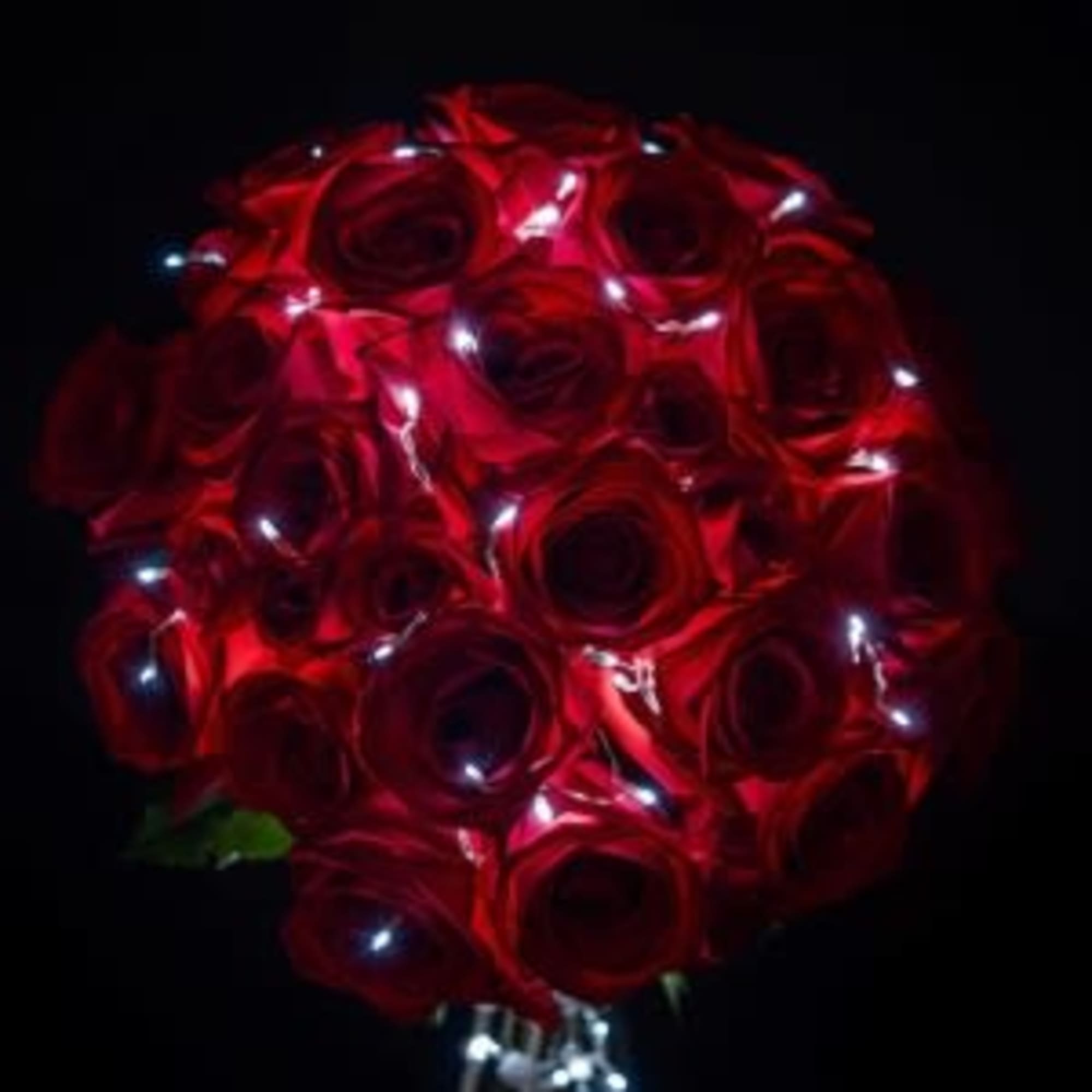 Tight bouquet of red roses accented with tiny white LED lights against a dark background