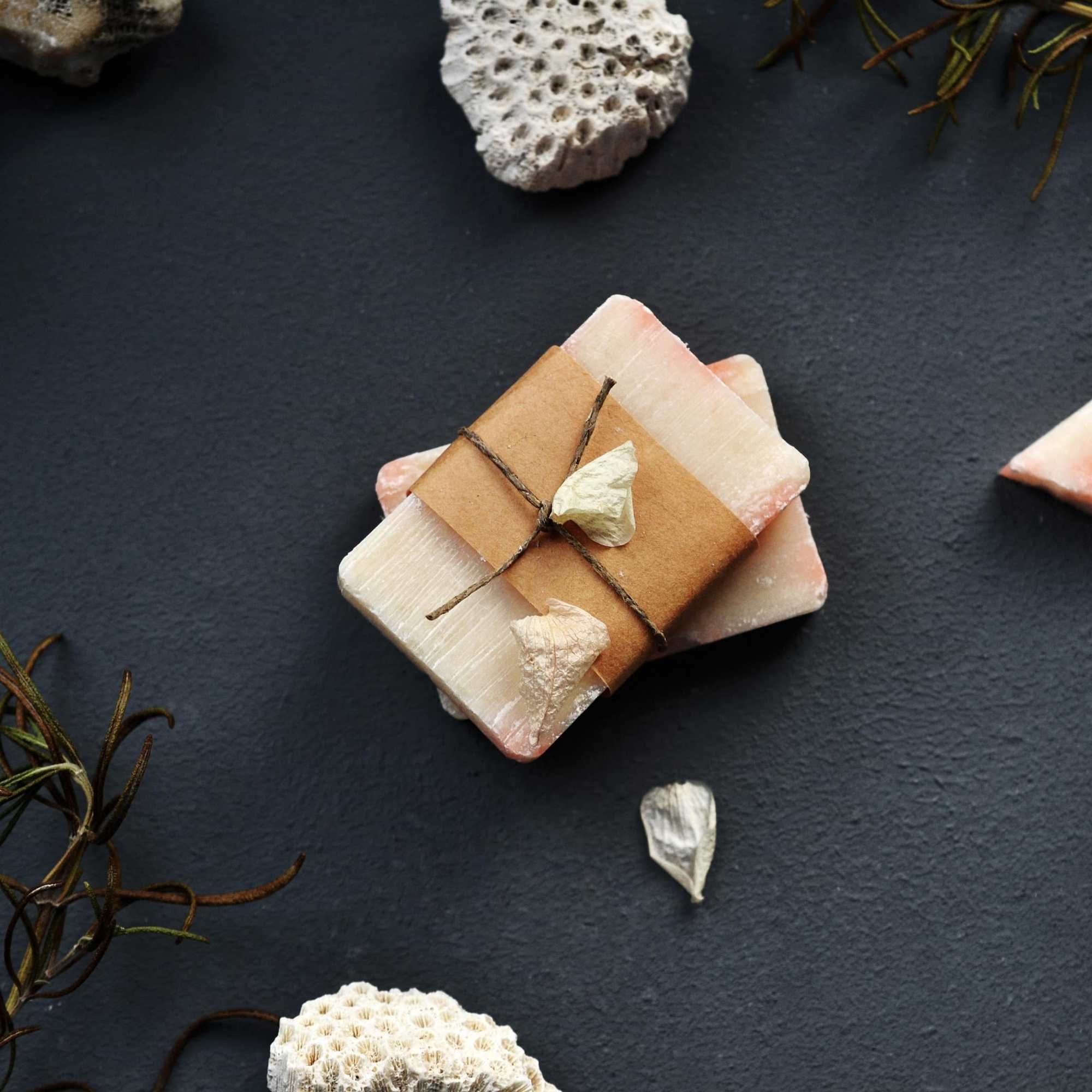 Stack of handmade soap bars wrapped in brown paper and twine on a dark surface with natural accents