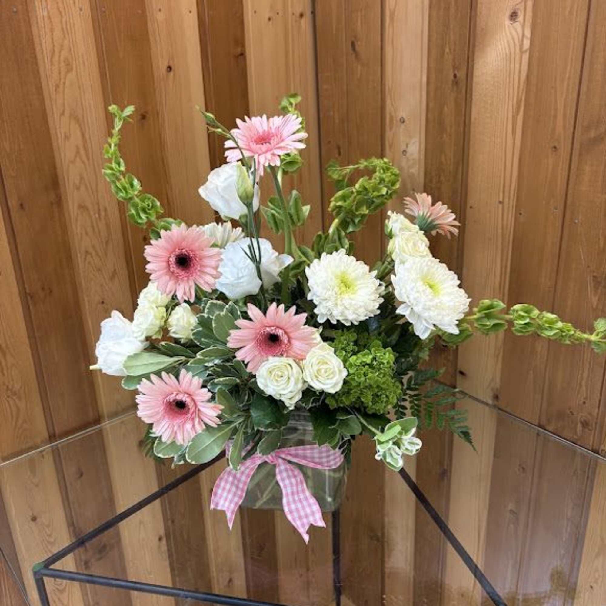 Pink gerbera daisies and white blooms in a glass vase with a pink gingham bow