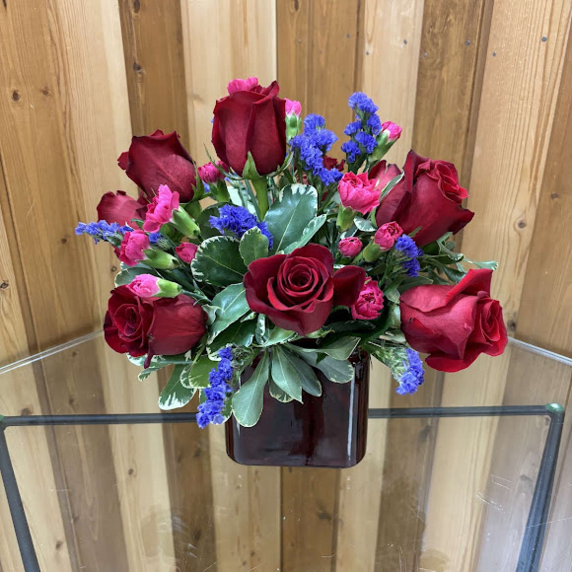 Red roses with pink carnations and purple accents in a dark red cube vase
