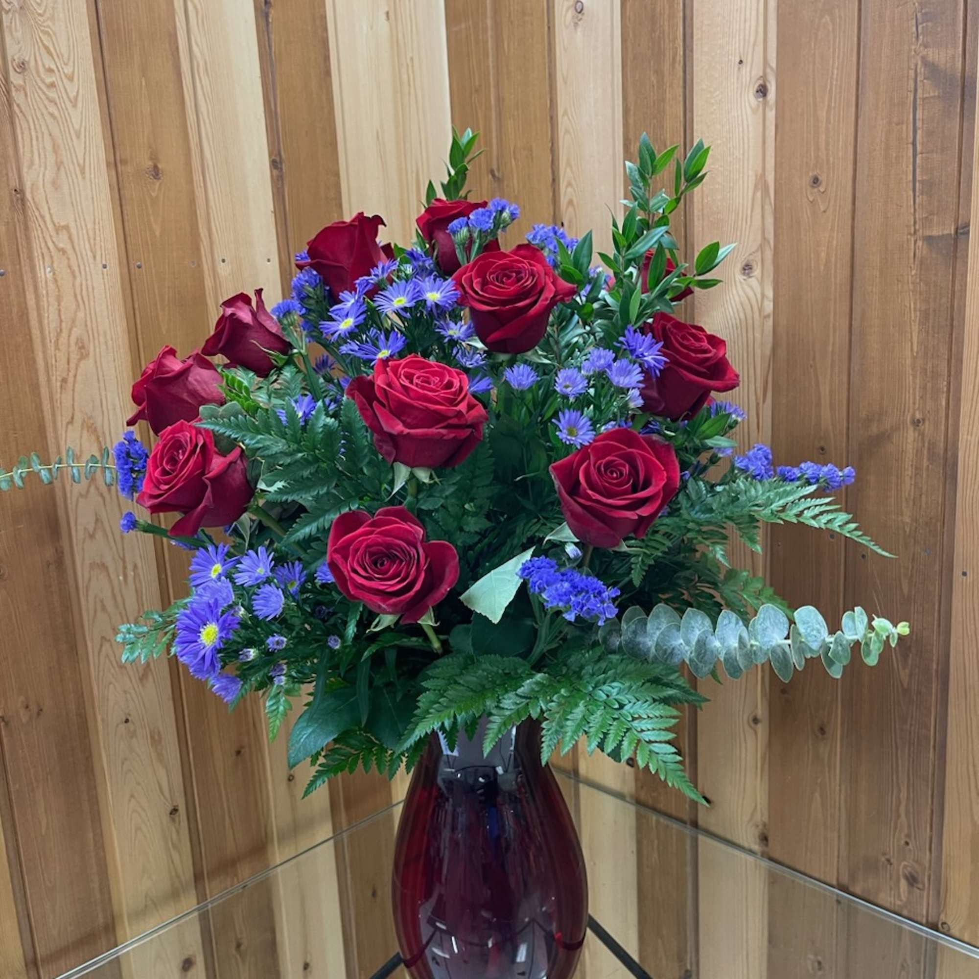 Arrangement of red roses and purple asters in a dark red glass vase