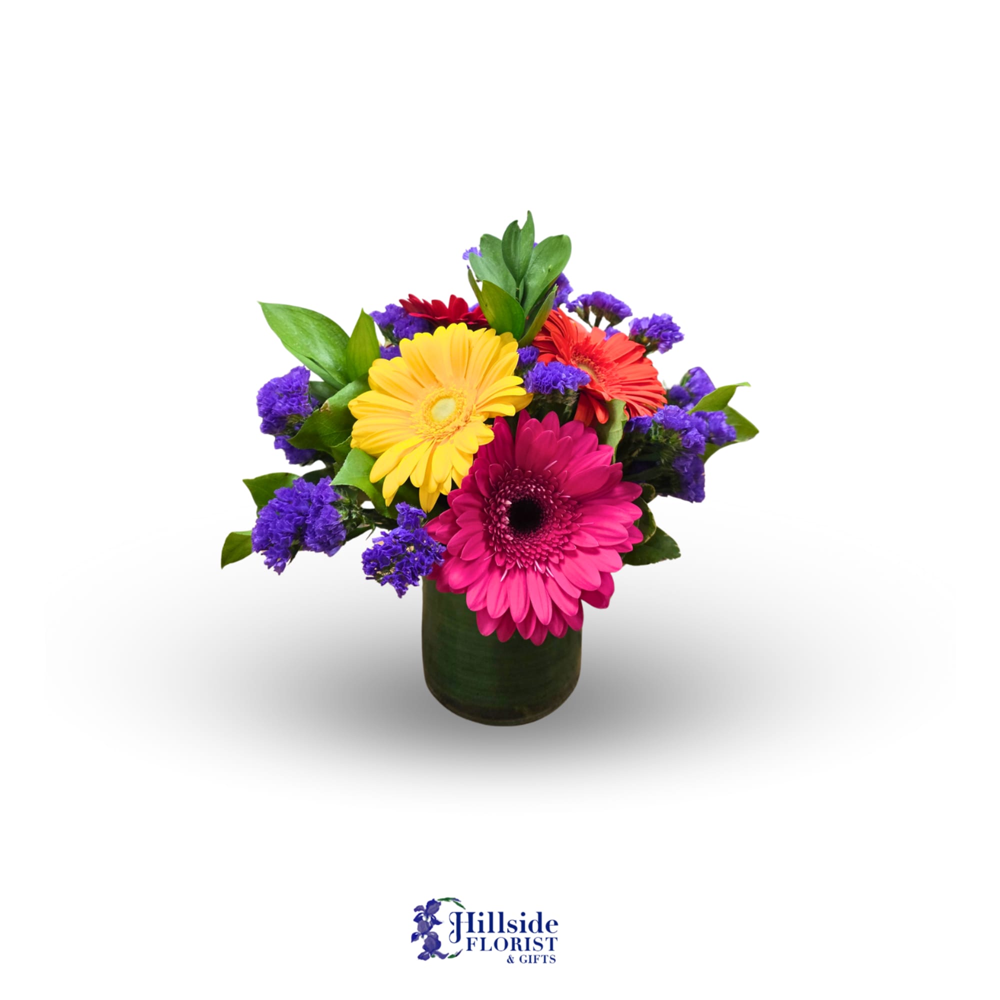 Bright mixed gerbera daisies with purple accents in a short green leaf-wrapped glass vase