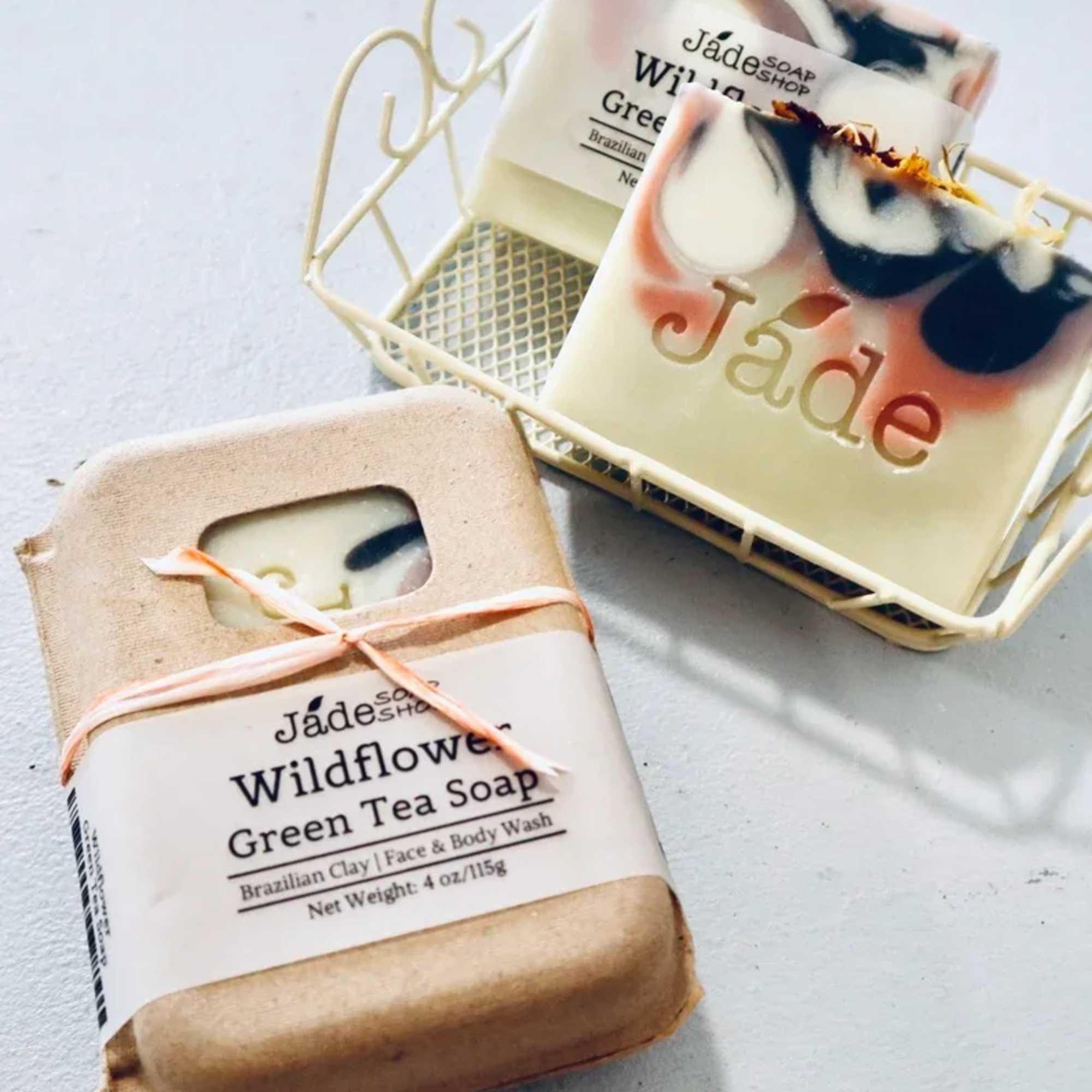 Artisan bar soaps with pink and black swirls, one wrapped in paper and one in a small cream metal tray.