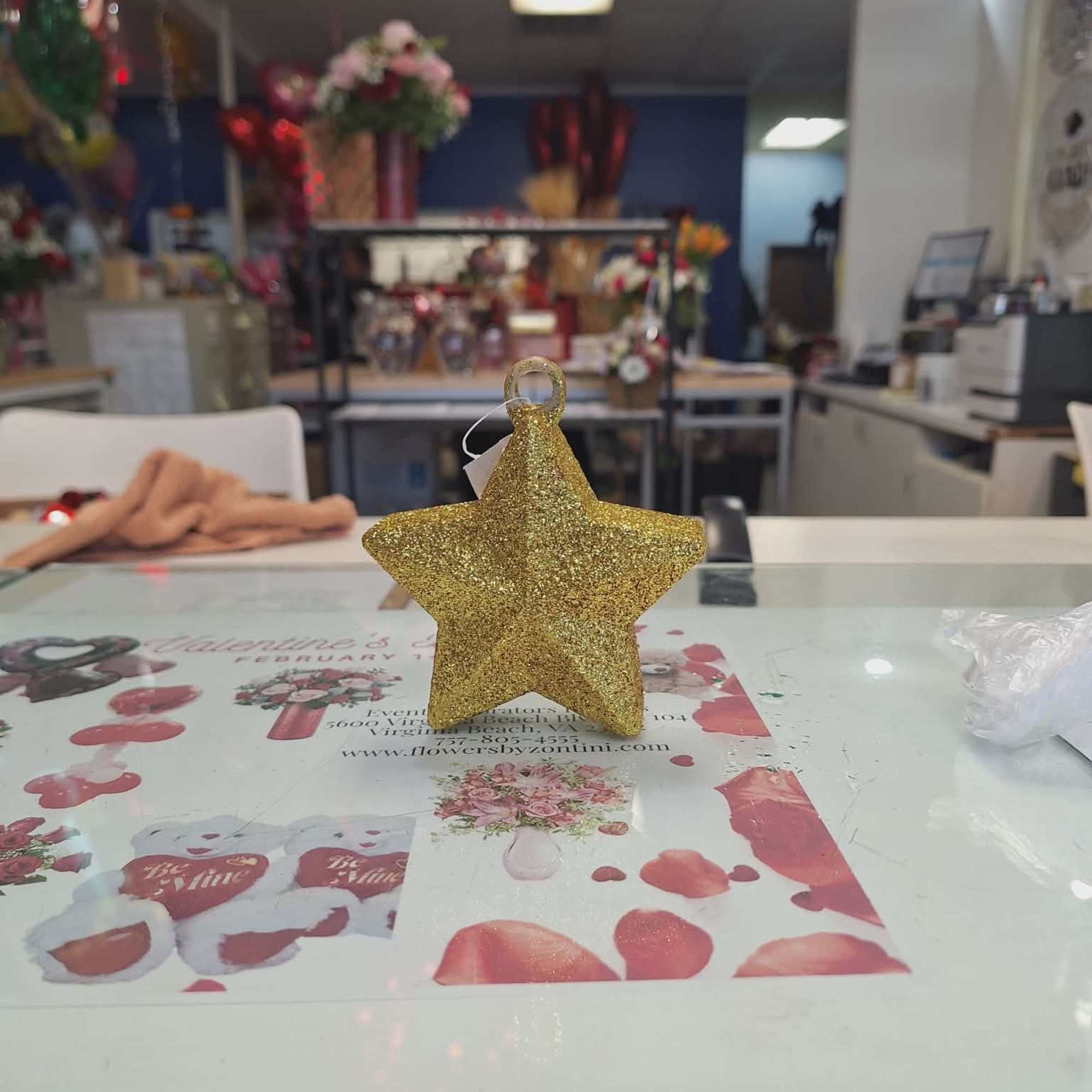 Gold glitter star ornament standing on a glass counter in a florist shop