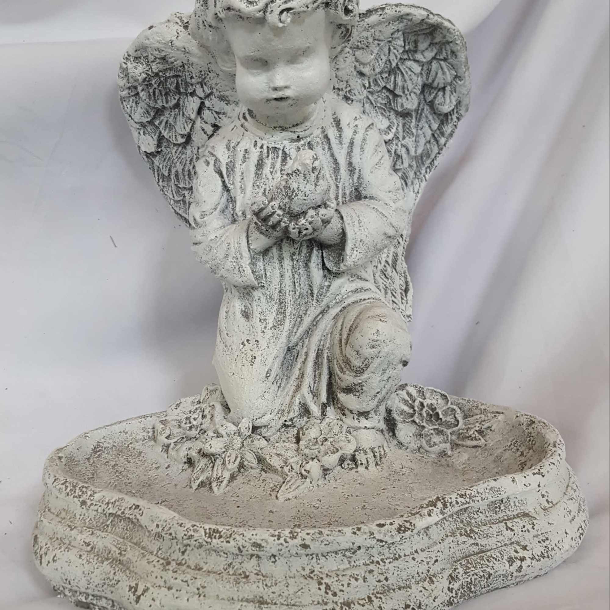 Kneeling stone angel figurine with wings on a shallow oval basin decorated with carved flowers.