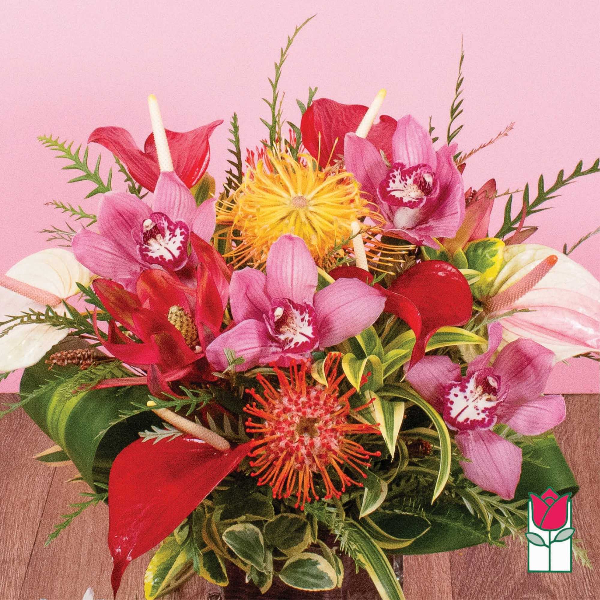 Tropical arrangement with pink orchids, red blooms, and yellow pincushion flowers in a low glass vase.