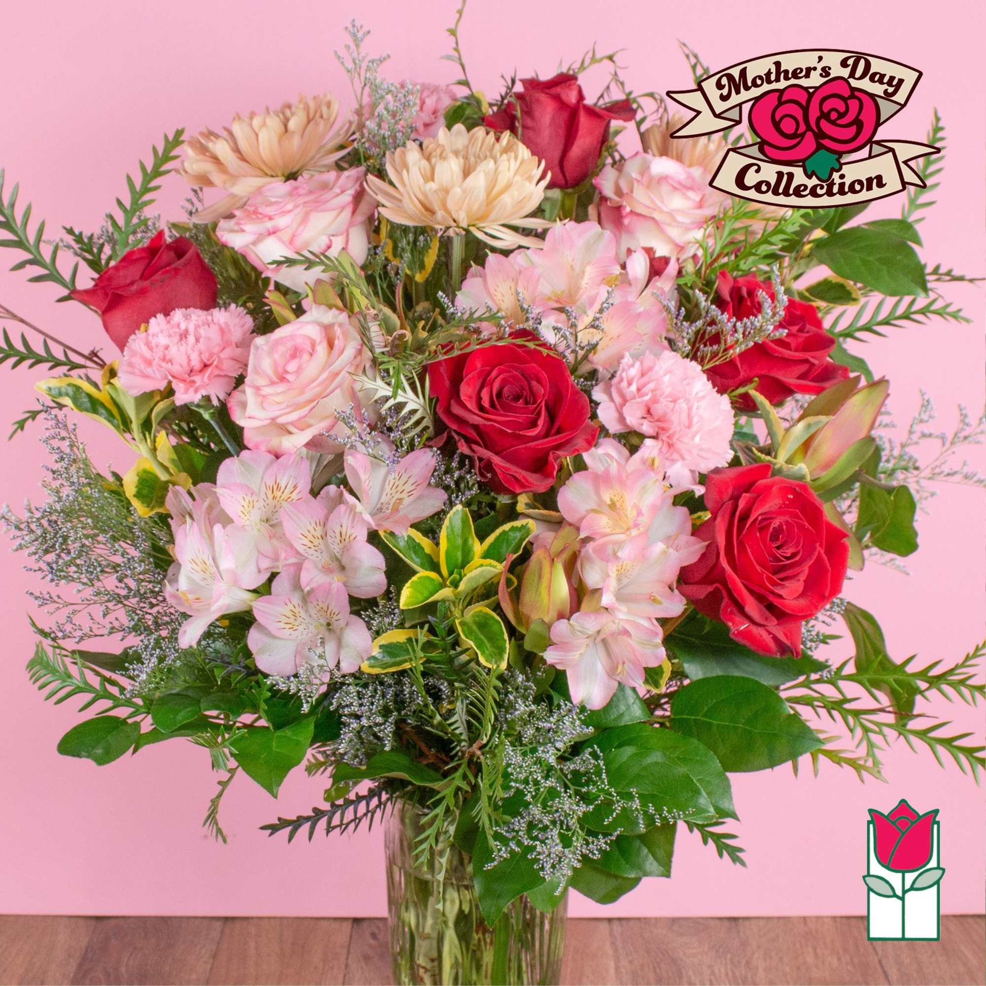Mixed bouquet of red roses, pink carnations, alstroemeria, and mums in a clear glass vase on a pink background