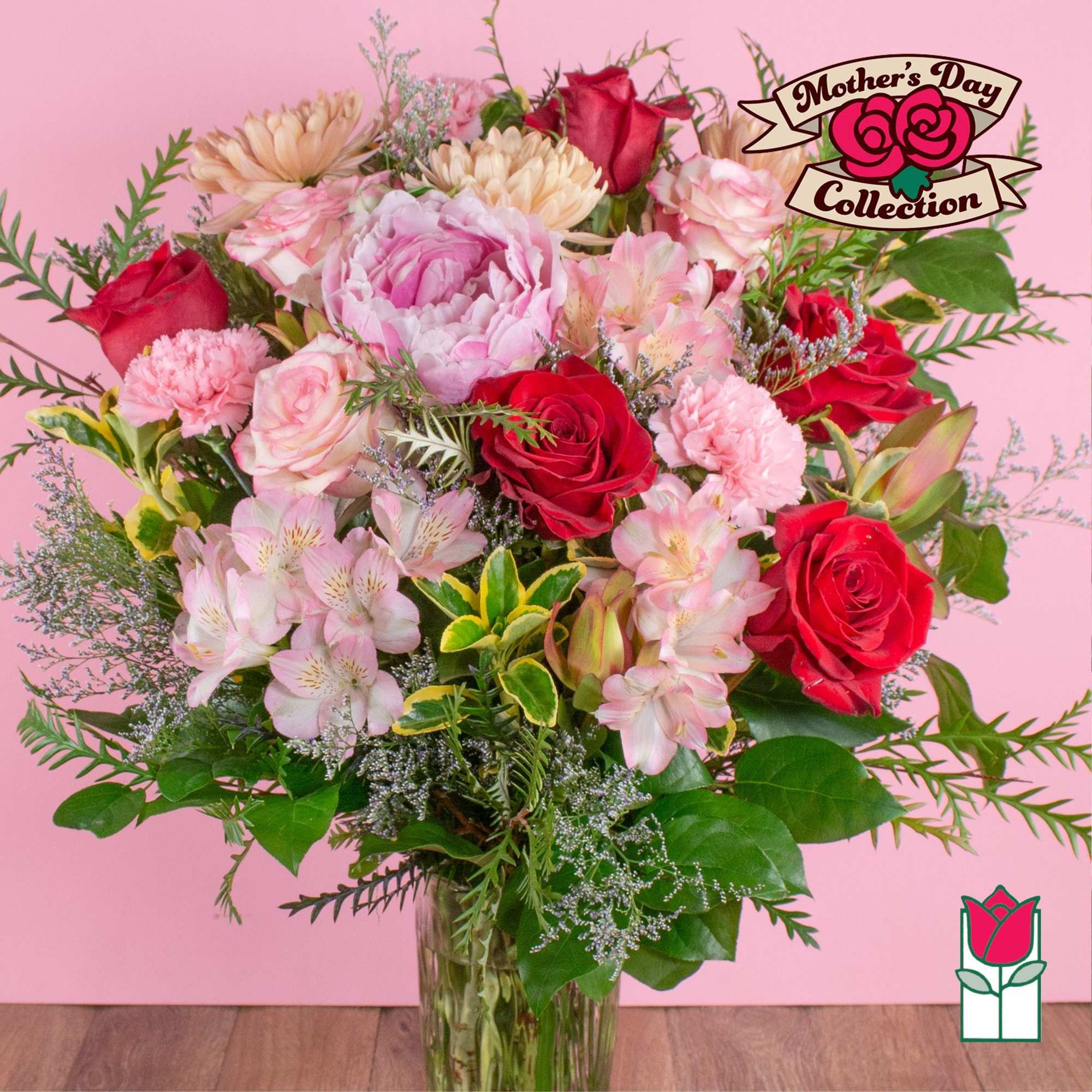Mixed bouquet of pink and red flowers including roses and peonies in a clear glass vase